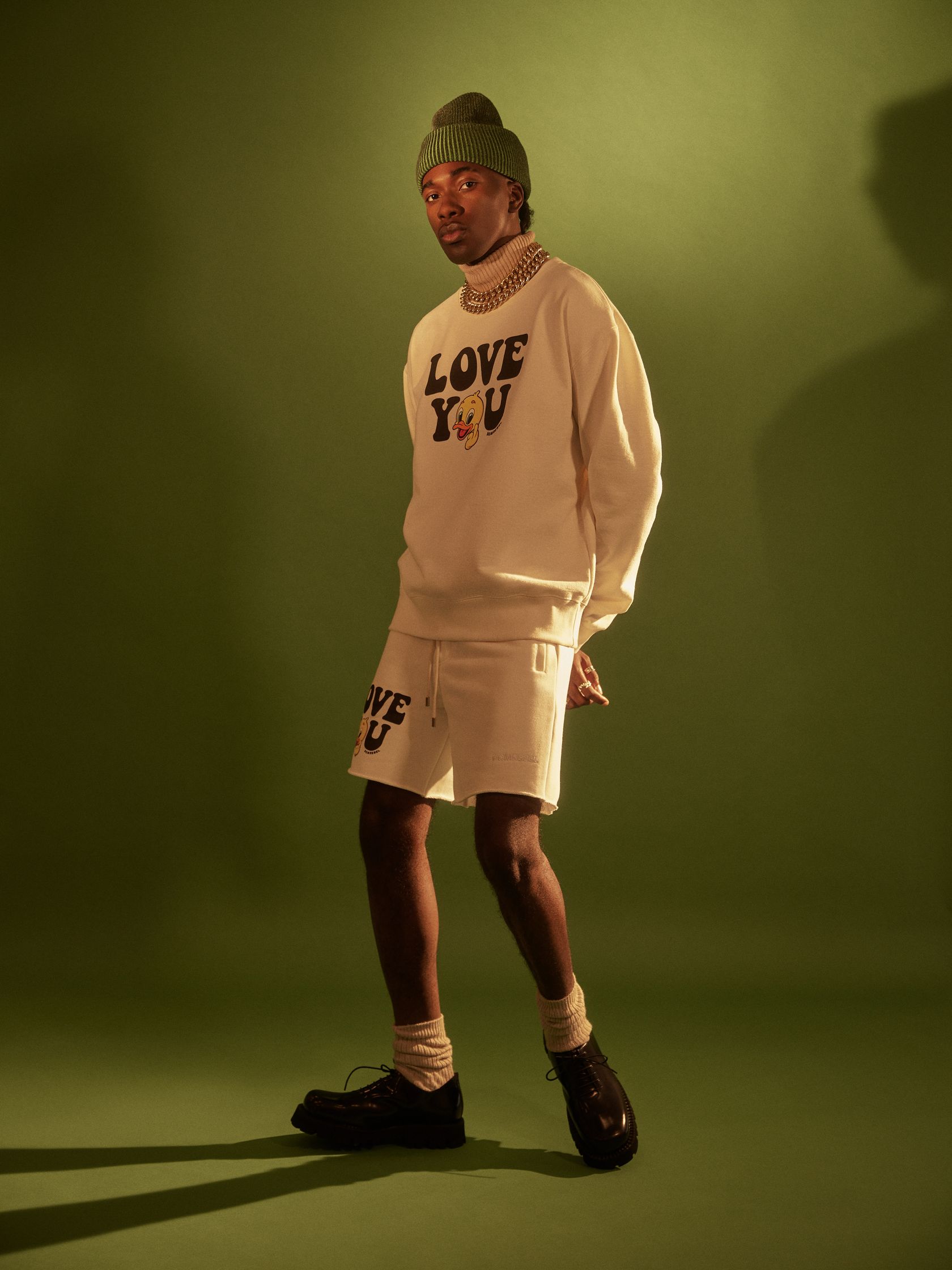 a man in a white sweater and shorts standing in front of a green background