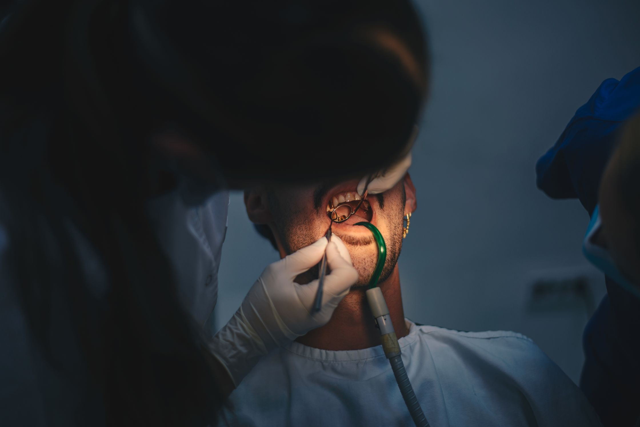 A dentist performing dental work on a patient's open mouth with specialized tools and bright light.