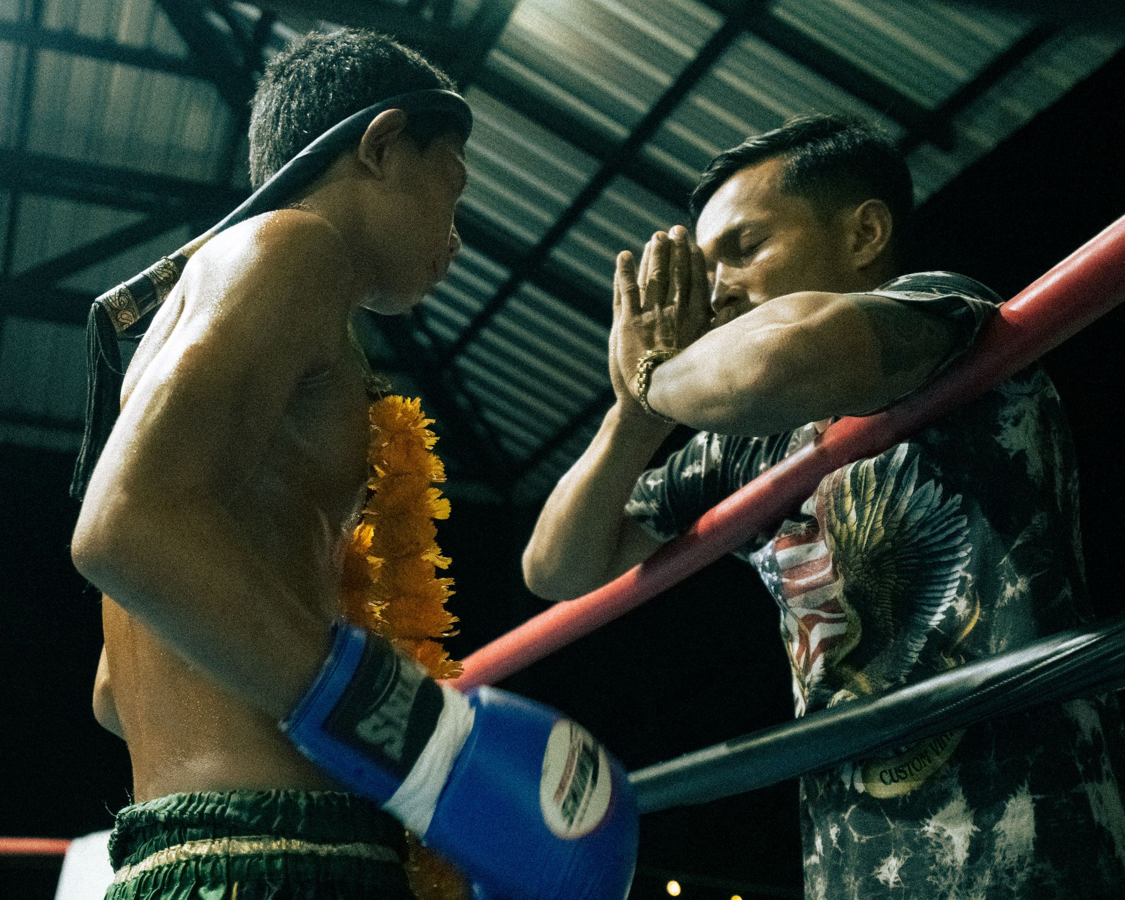 A Muay Thai coach performing a respectful Wai gesture in front of the fighter before the fight in the ring of Koh Tao.