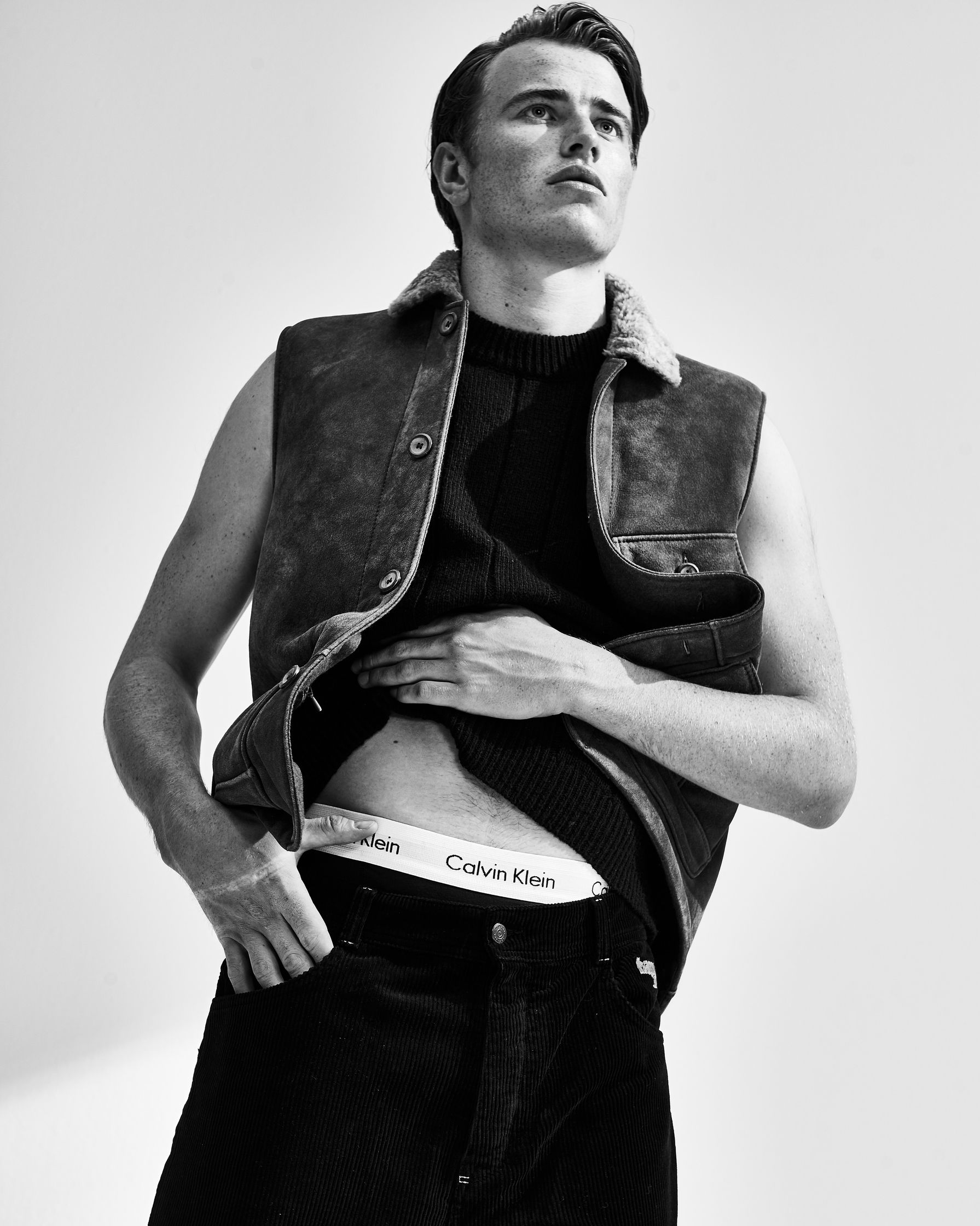 a black and white photo of a man in a vest and jeans