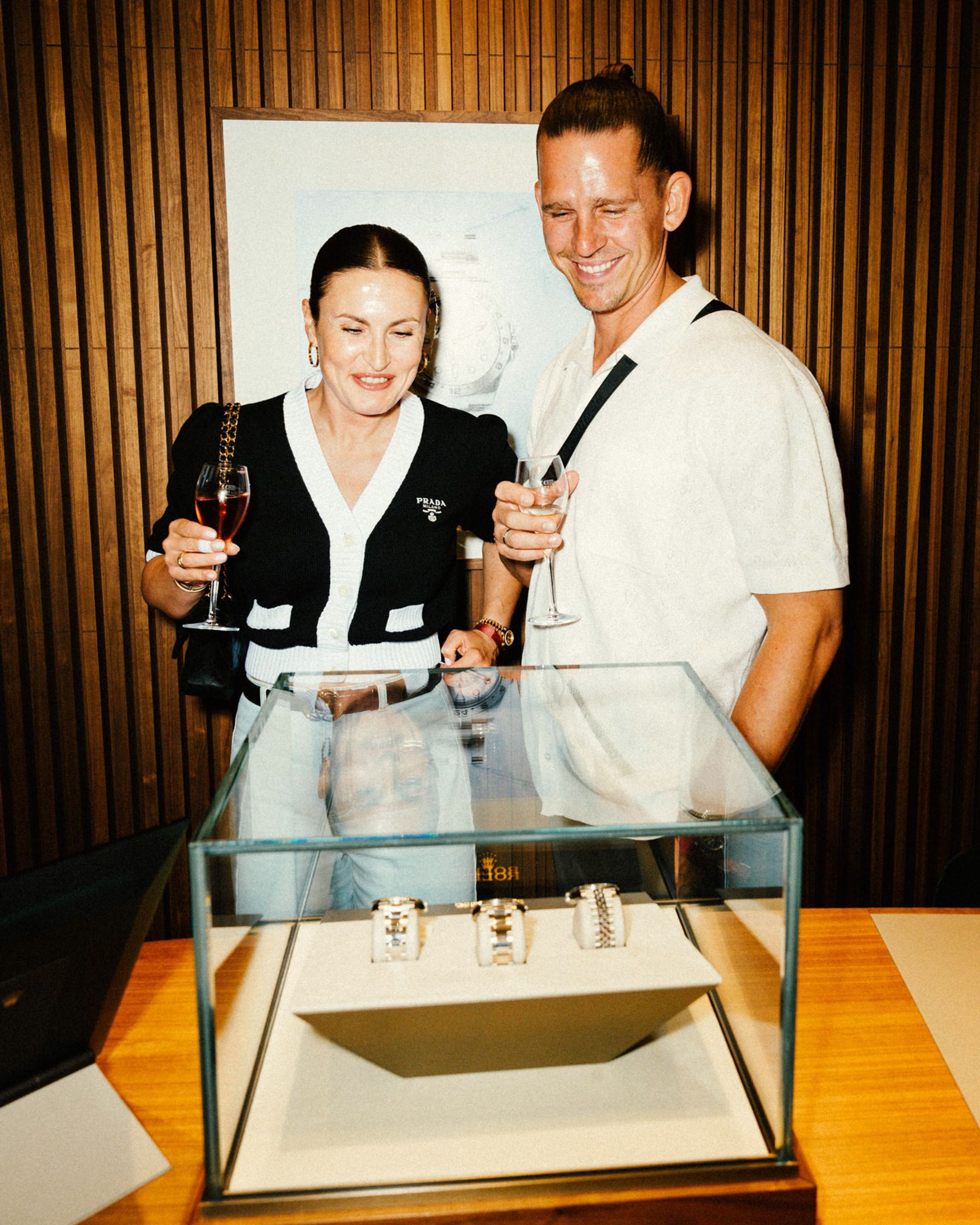 Frau in Prada-Cardigan und Mann im weißen Polo betrachten lächelnd eine Rolex-Vitrine mit Uhren beim Rolex Boutique Event Berlin
