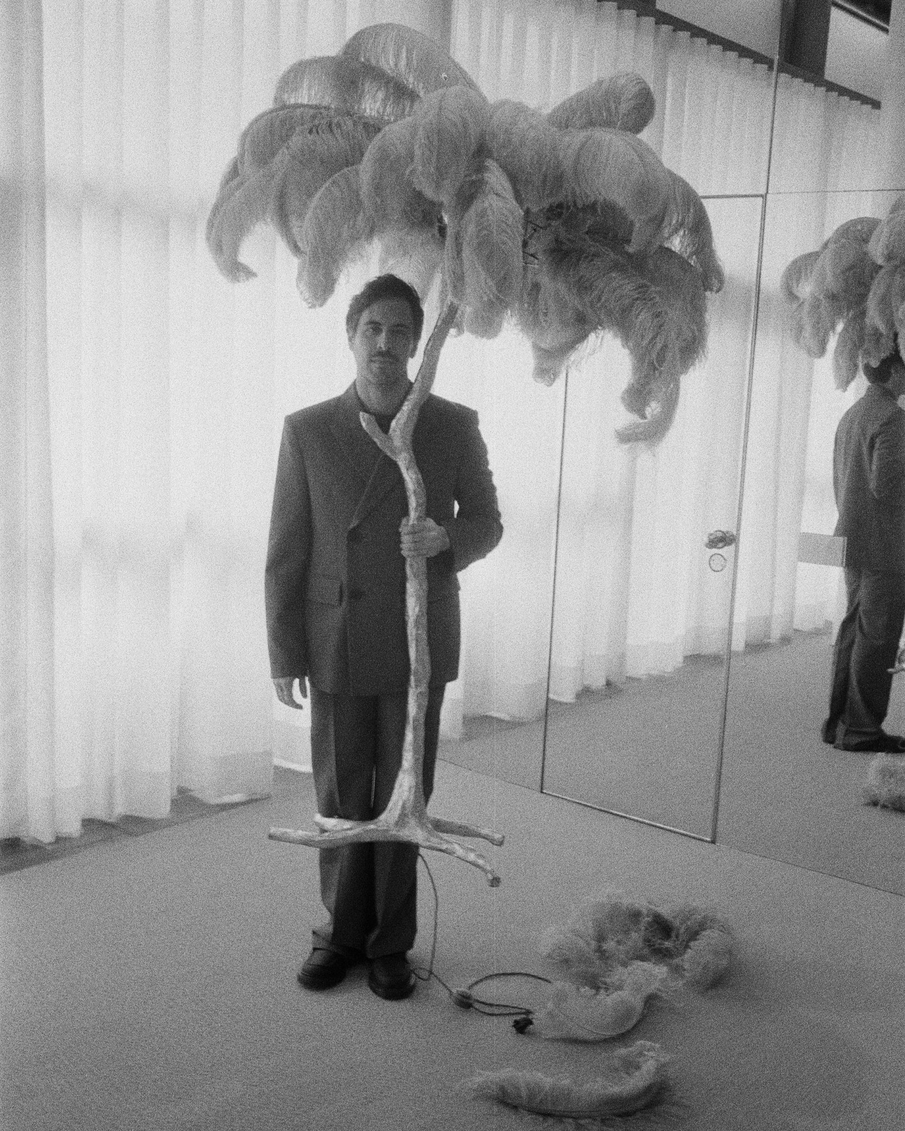 Max Giesinger in a suit standing next to a feathered tree