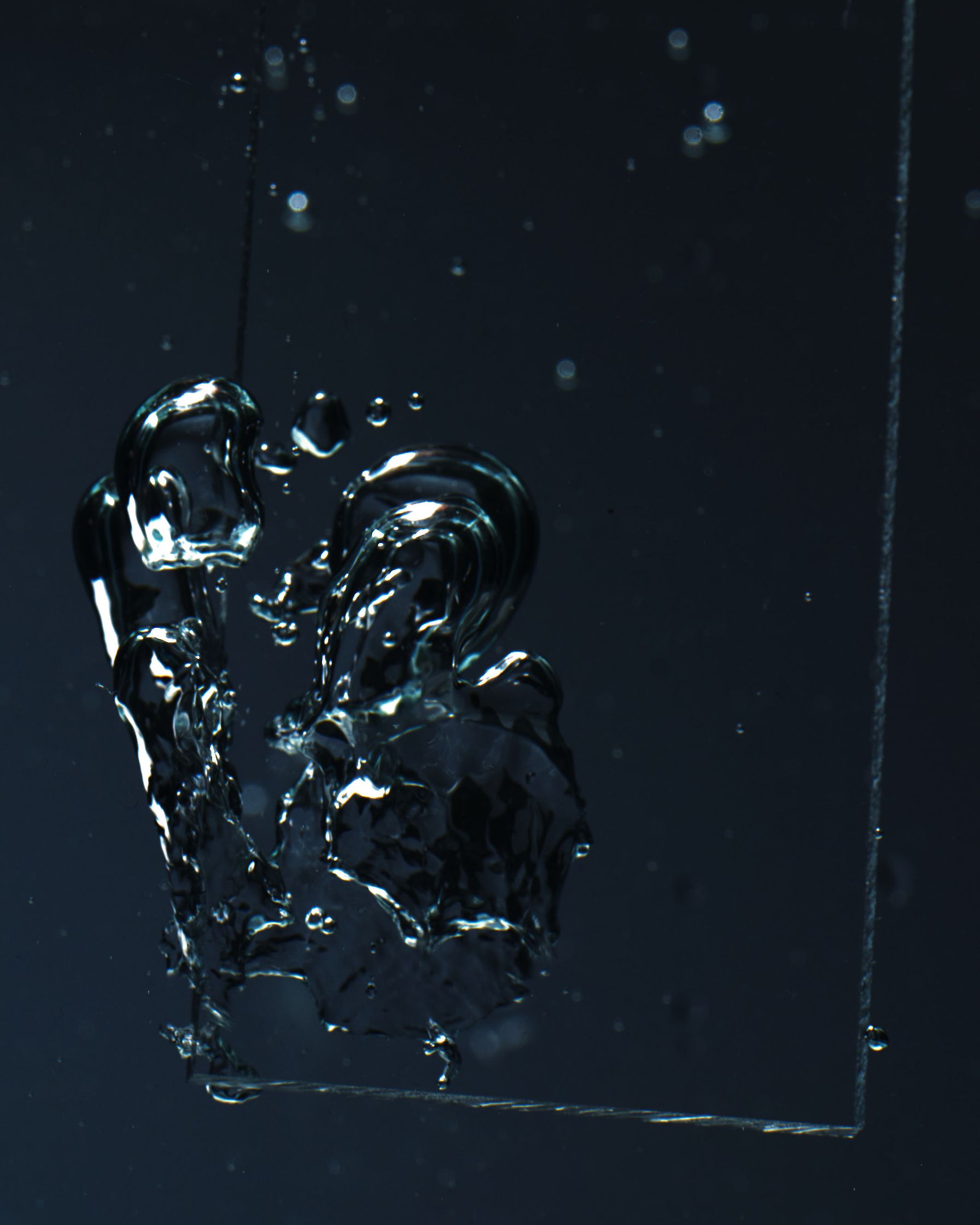 Piece of glass submerged in water, capturing abstract splash with light reflections.