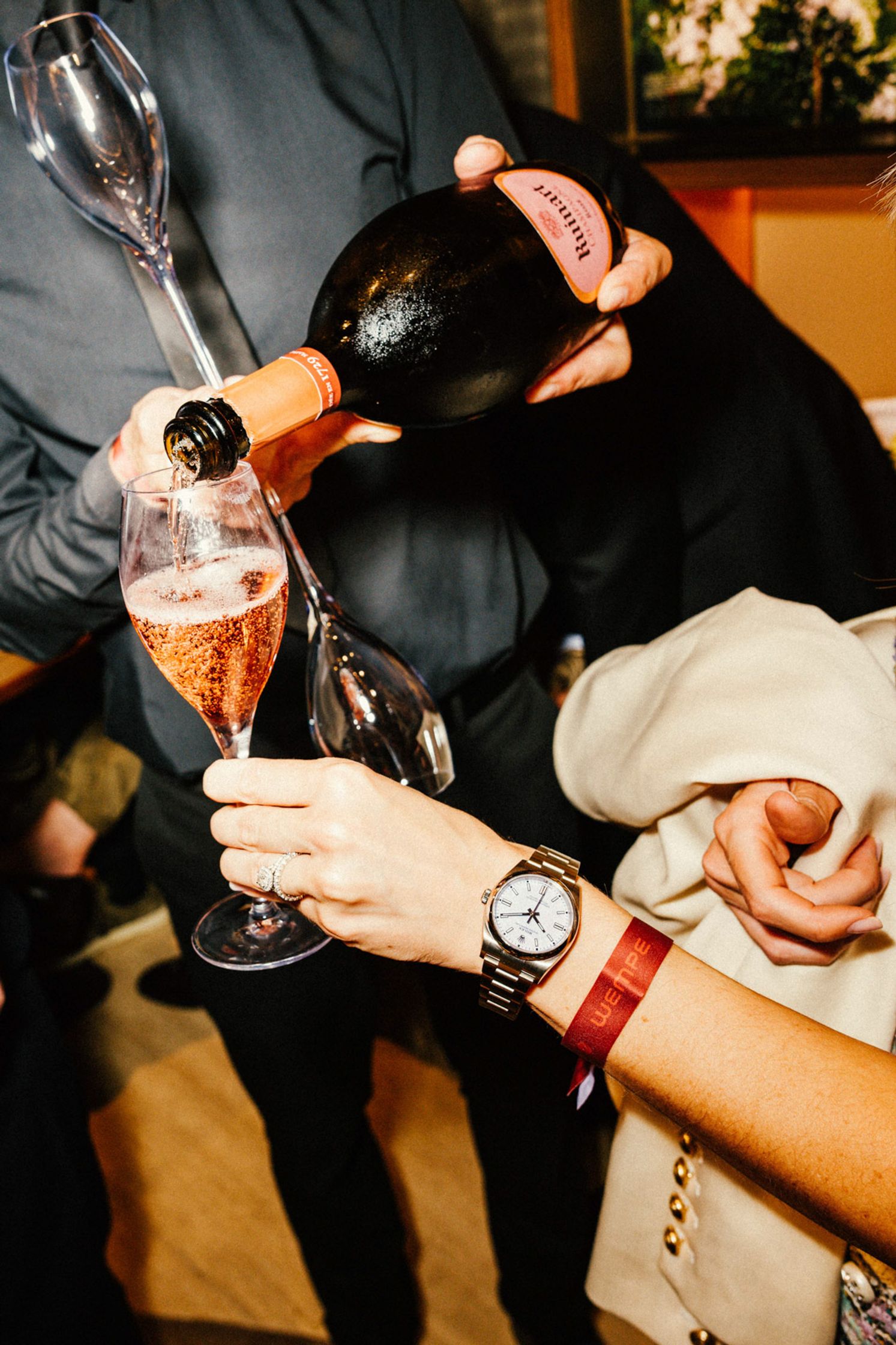 Rosé-Champagner wird aus einer dunklen Flasche in ein Sektglas gegossen, Rolex-Uhr am Handgelenk der Person gut sichtbar, festliche Stimmung beim Rolex Boutique Berlin Event