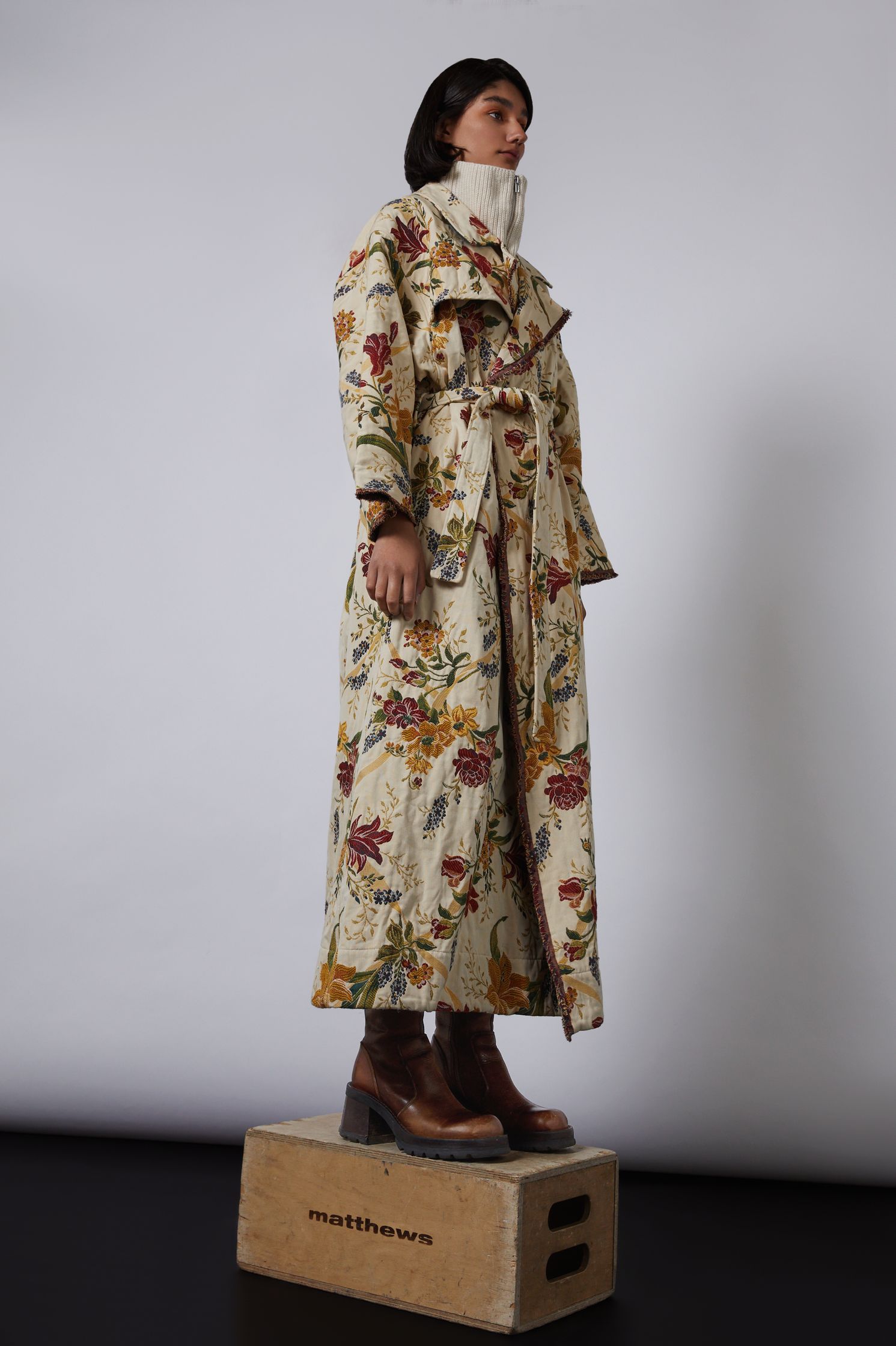 a model wearing a floral coat standing on a wooden box