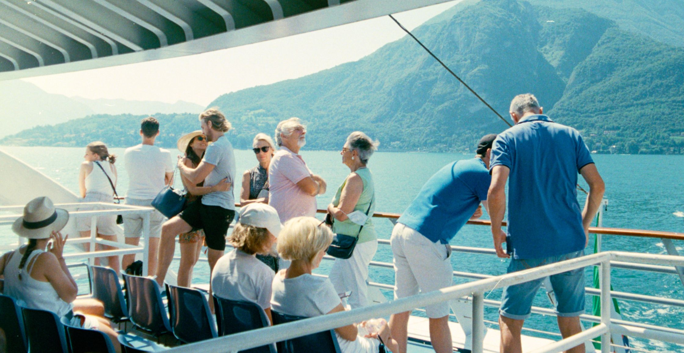 A candid scene on a ferry crossing Lake Como, featuring couples of different ages and groups of friends enjoying the Italian summer light.