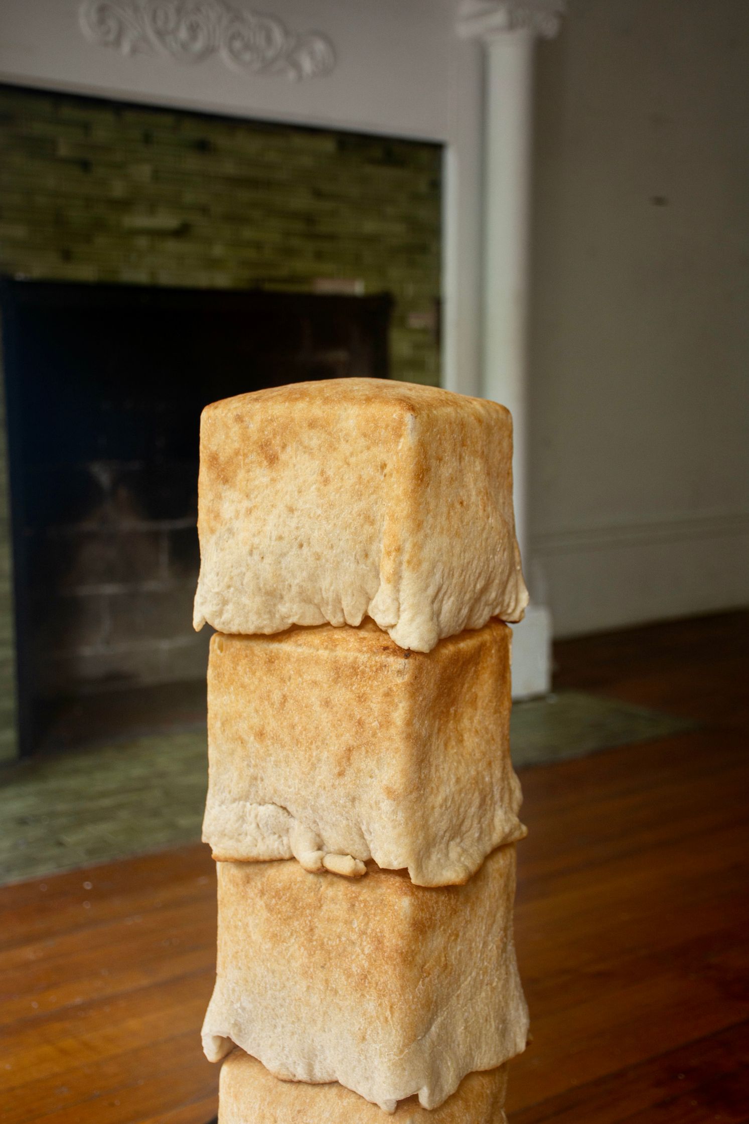 A tall stack of pale, square bread loaves sits in front of a white fireplace with a dark brick interior.