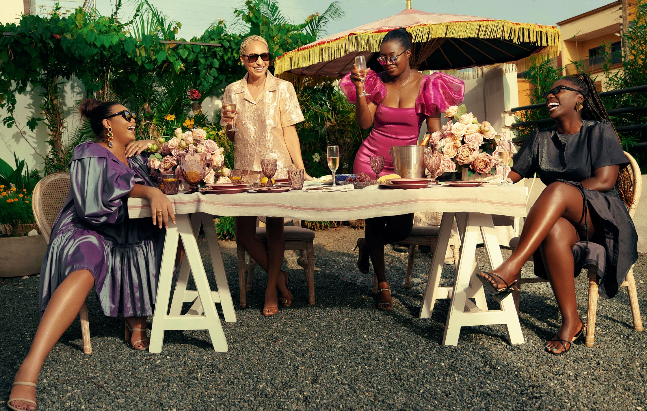 fashion editorial shoot of a group of women sitting at a table with food , flowers and wine. which was set to represent the last supper 