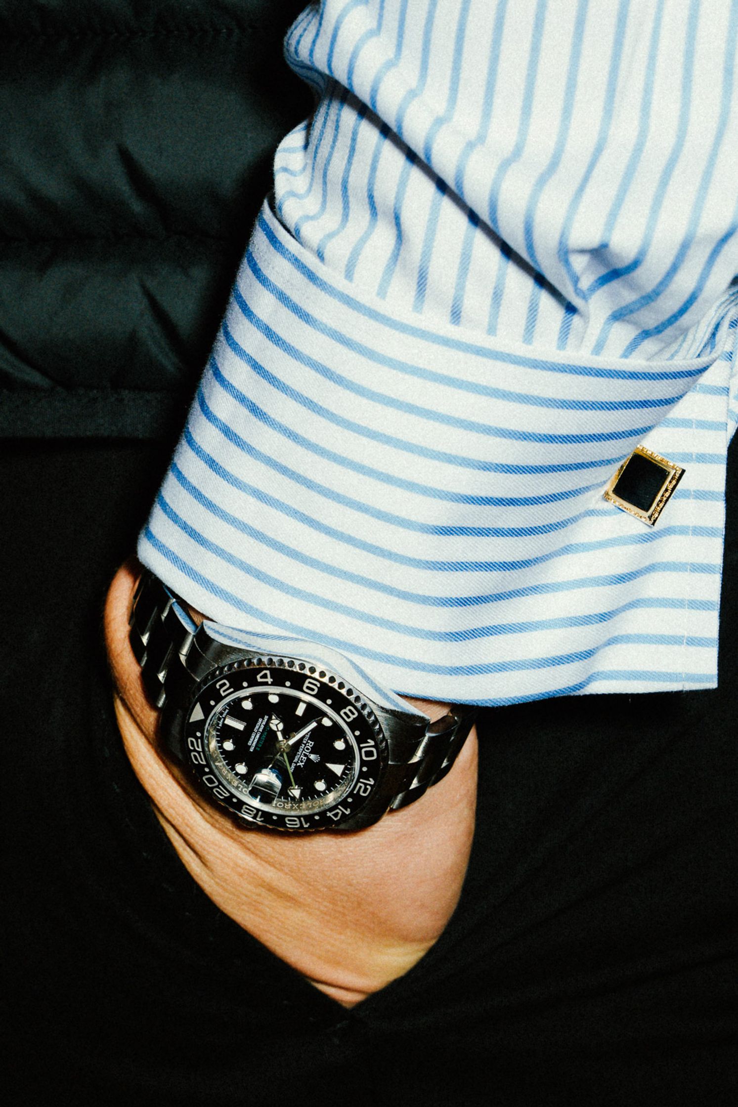 Stilvolle Nahaufnahme: Schwarze Rolex GMT-Master II am Handgelenk eines Herrn im blau-gestreiften Hemd mit goldenen Manschettenknöpfen beim Rolex Boutique Event Berlin