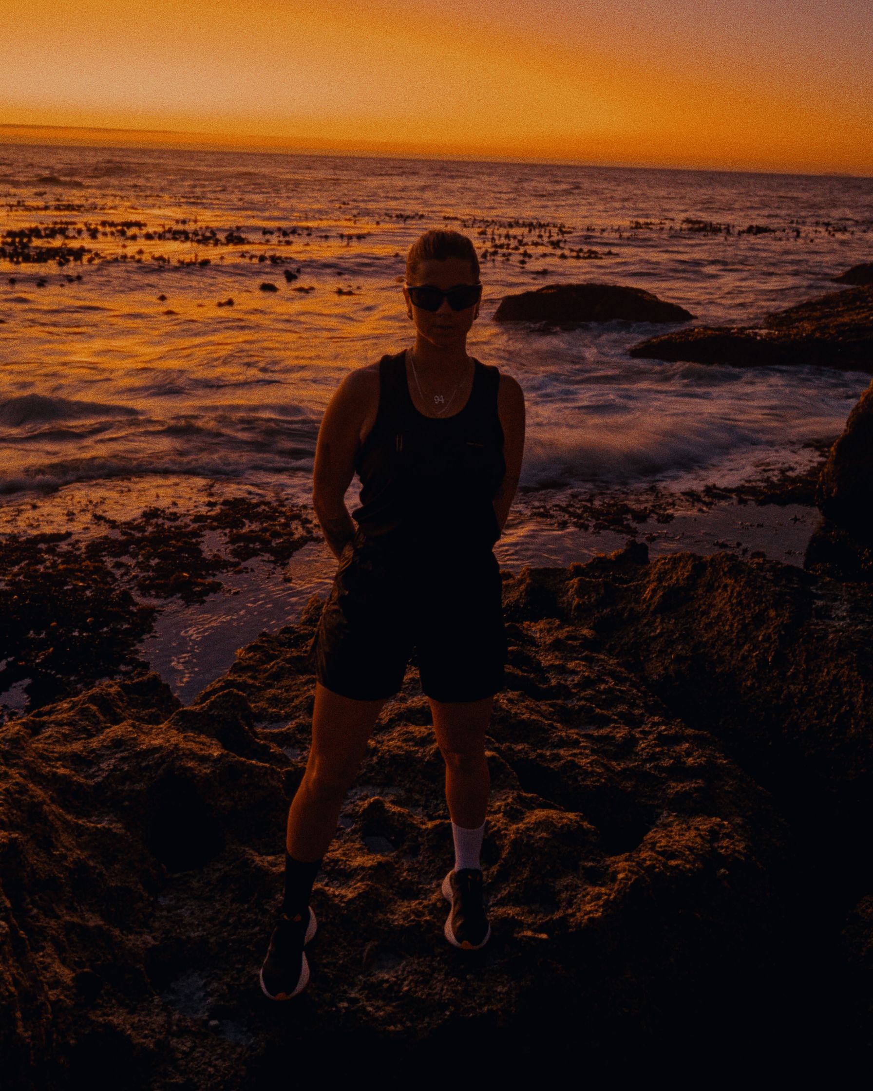 a woman standing on rocks at sunset
