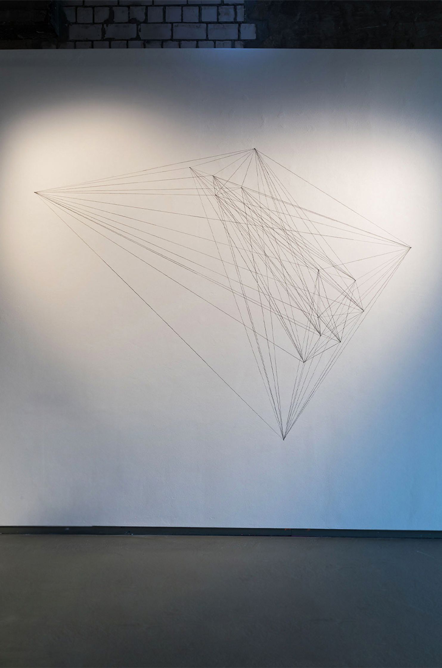 A complex string art installation forms geometric shapes on a white wall.