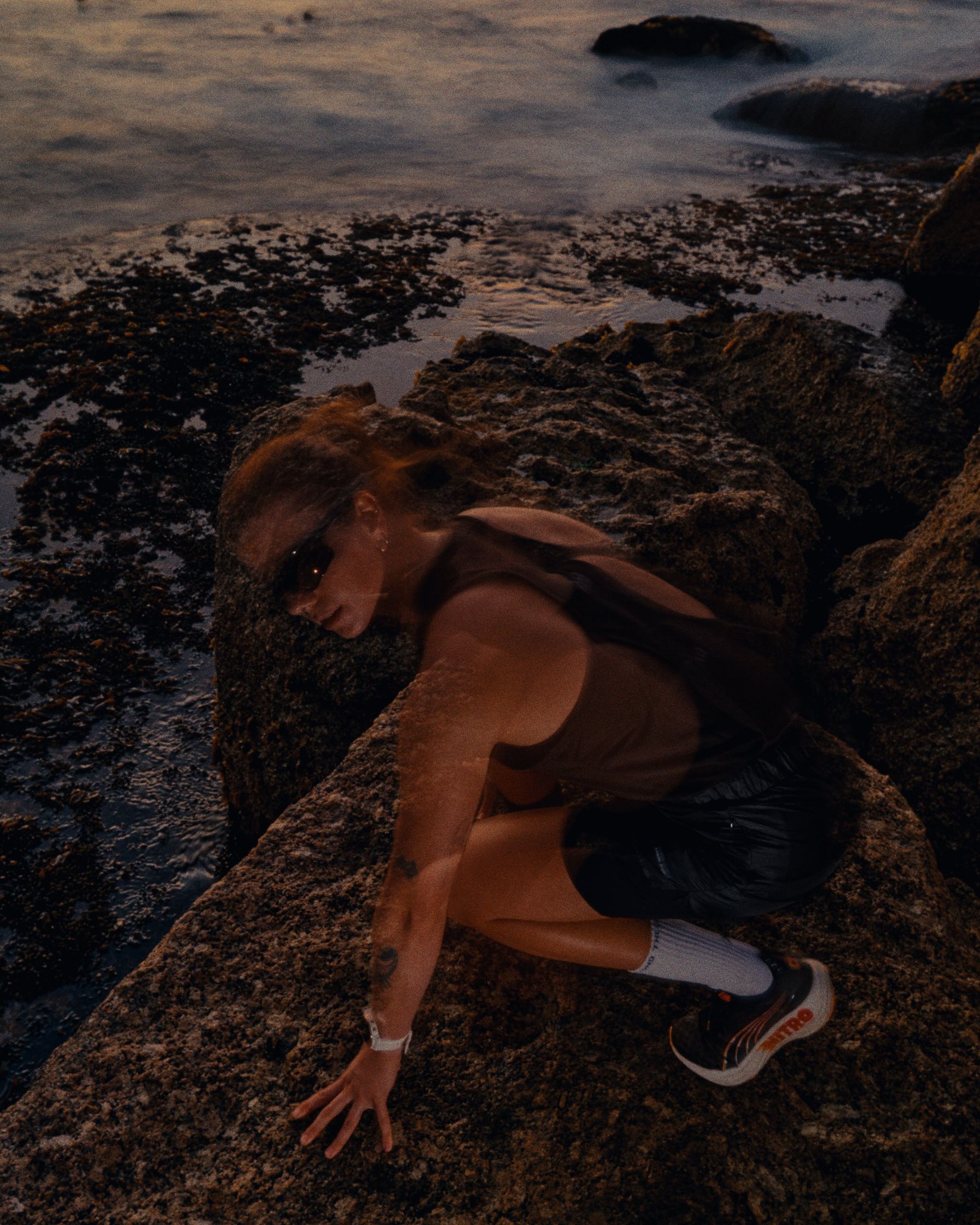 a woman crouching on rocks near the ocean