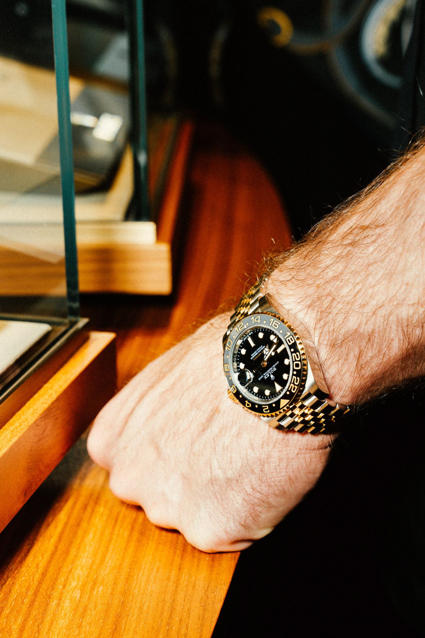 Nahaufnahme: Rolex GMT-Master II in Gold mit schwarzem Zifferblatt und Jubilee-Armband am Handgelenk, ruhend auf einem warmen Holztresen in der Rolex Boutique Berlin