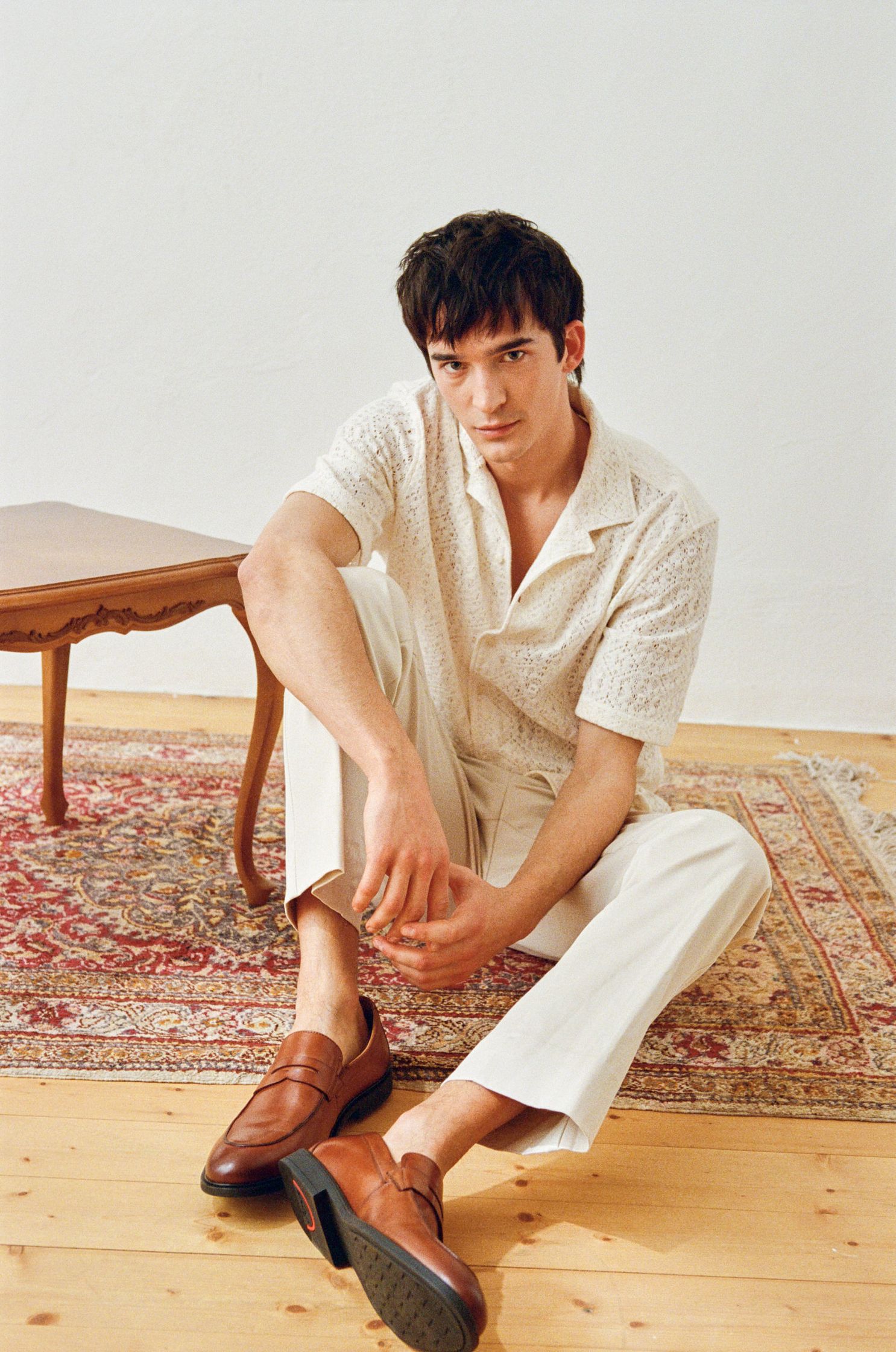 a man sitting on the floor in a white shirt and brown shoes