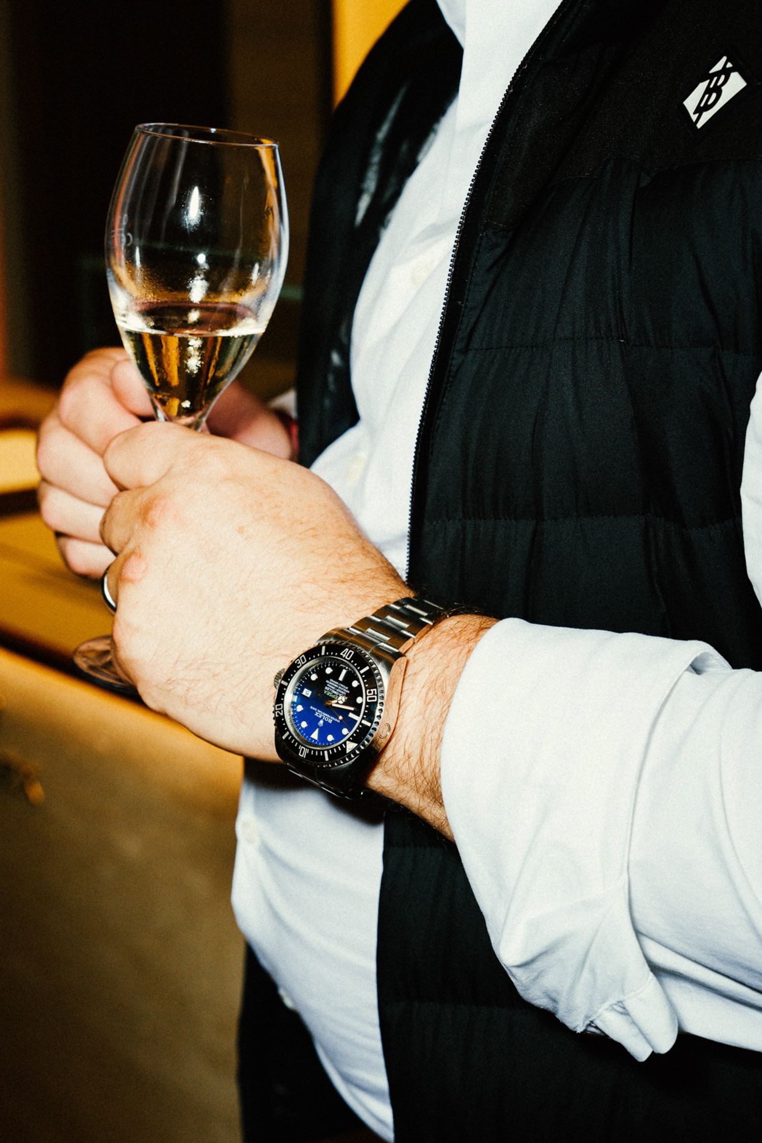Mann im dunklen Anzug mit Einstecktuch hält ein Weinglas, blaue Rolex-Uhr am Handgelenk sichtbar, Lifestyle-Event Rolex Boutique Berlin