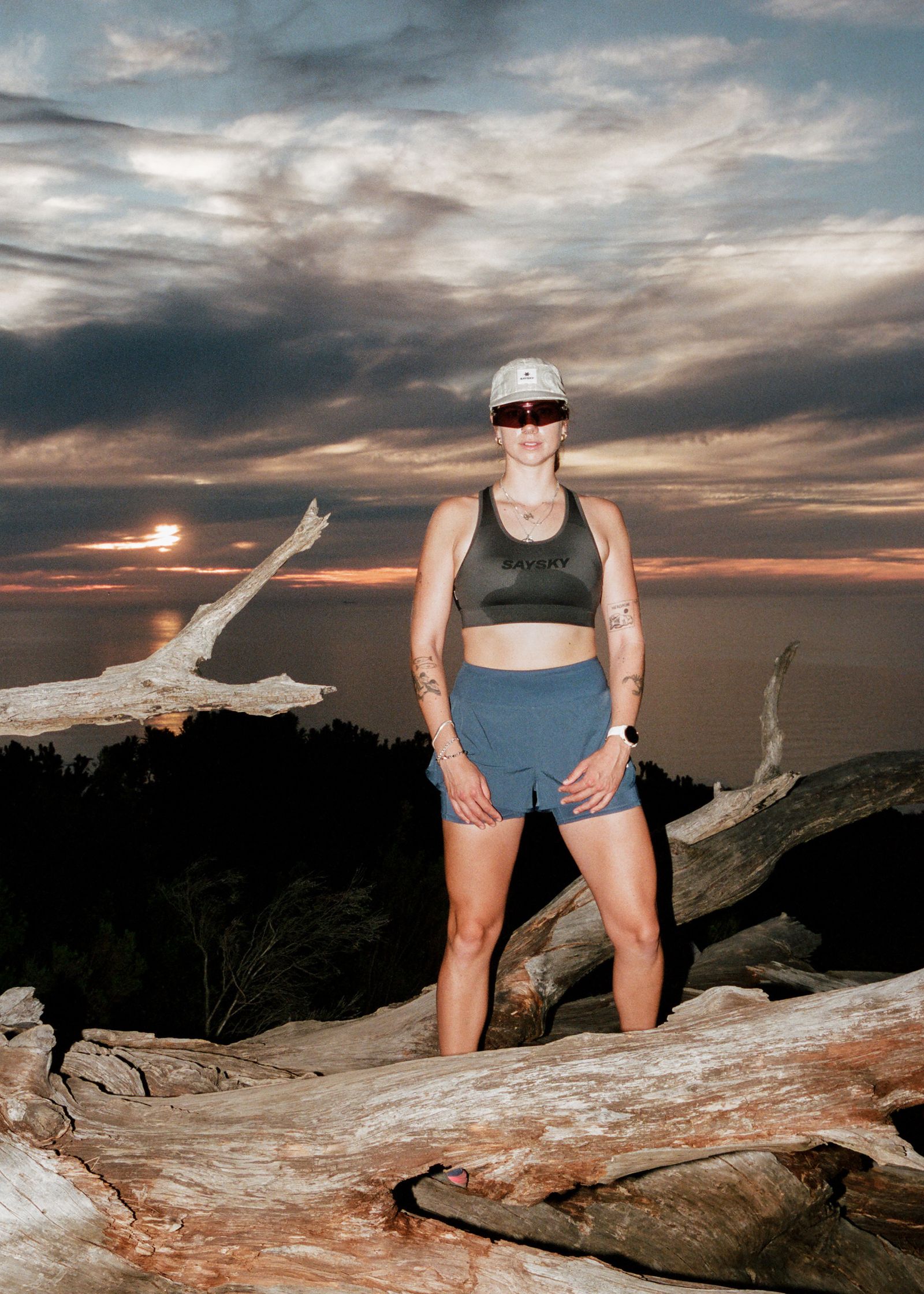 a woman standing on top of a fallen tree at sunset