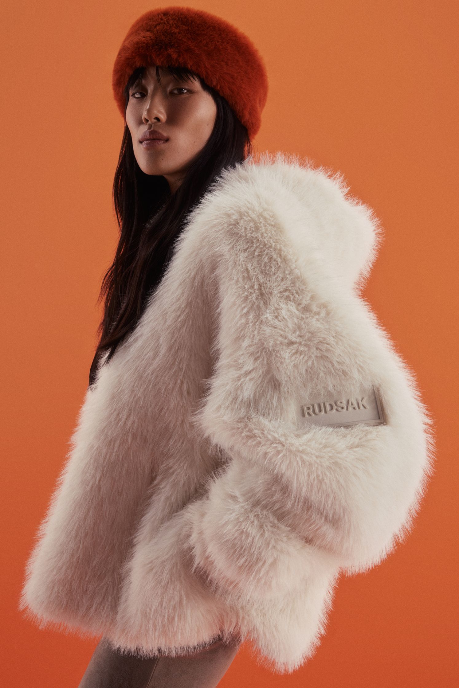 a woman in a white fur coat posing on an orange background