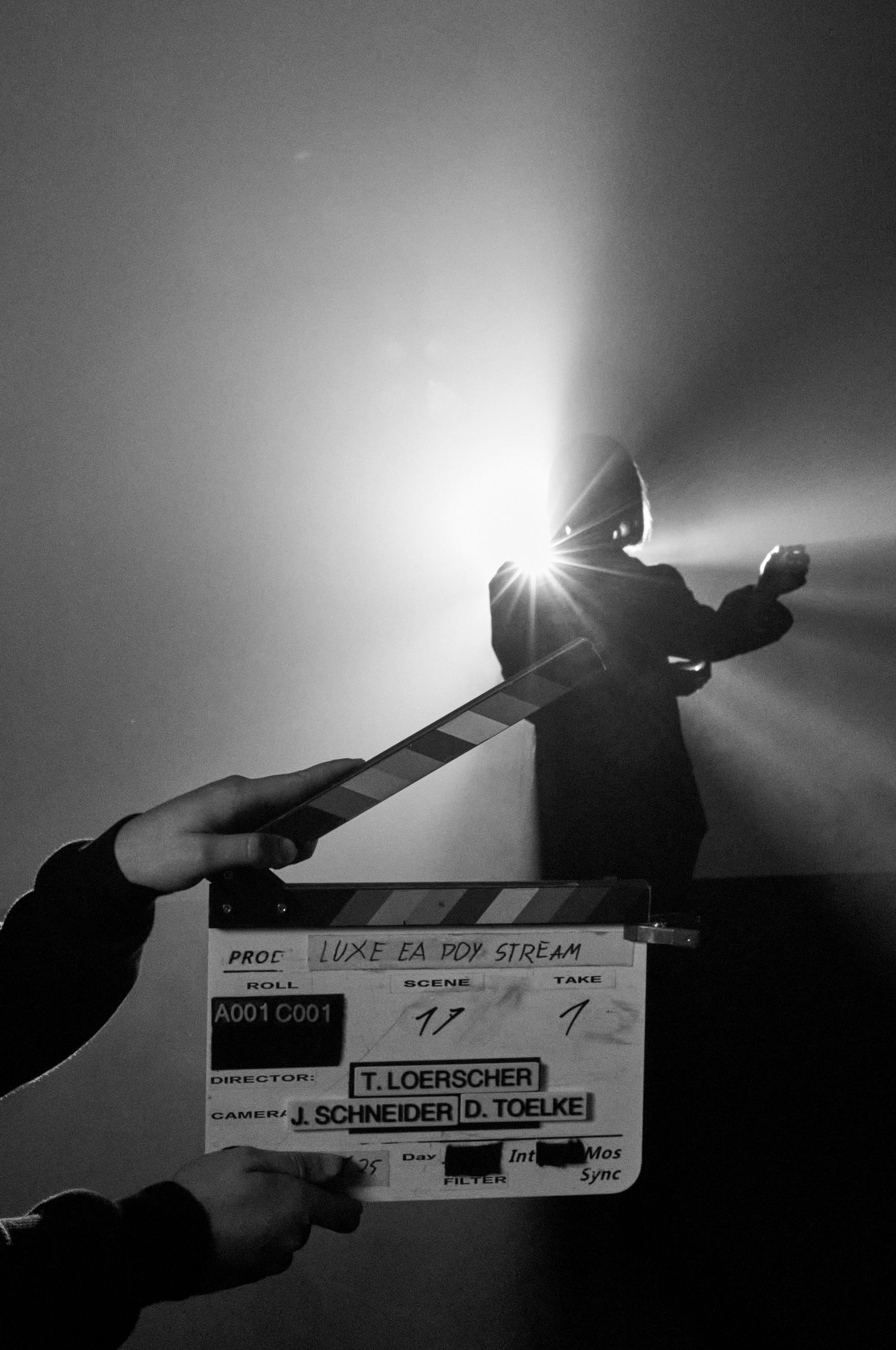 Filmklappe vor einer im Gegenlicht stehenden Person, Lichtstrahlen brechen durch den Kopf der Silhouette, Schwarzweiß-Fotografie