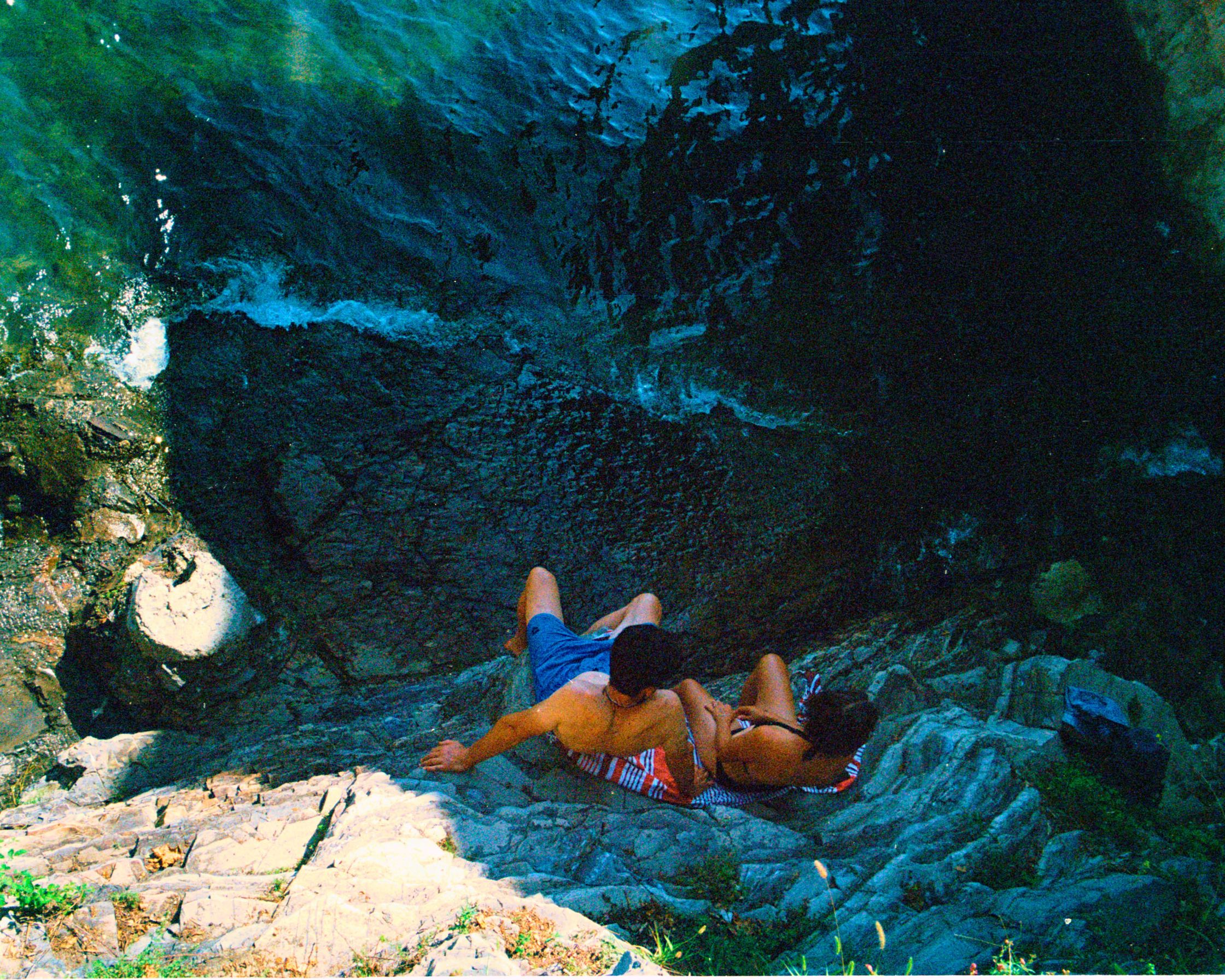 "A young couple seeking shade from the bright summer sun and the crowds by the sea at Lake Como, Italy. A candid moment of intimacy and quiet retreat.