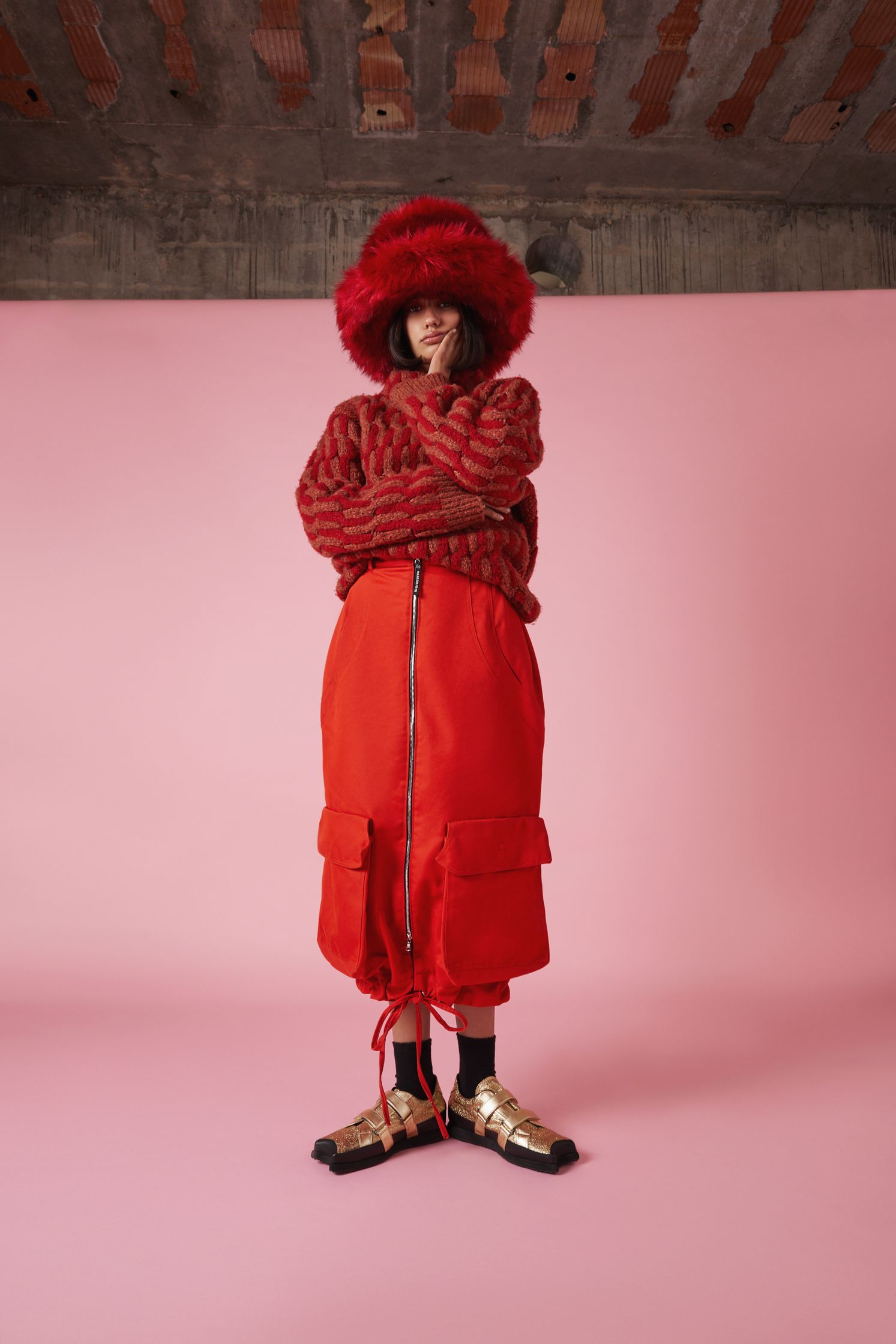 a woman in a red skirt and hat standing in front of a pink wall