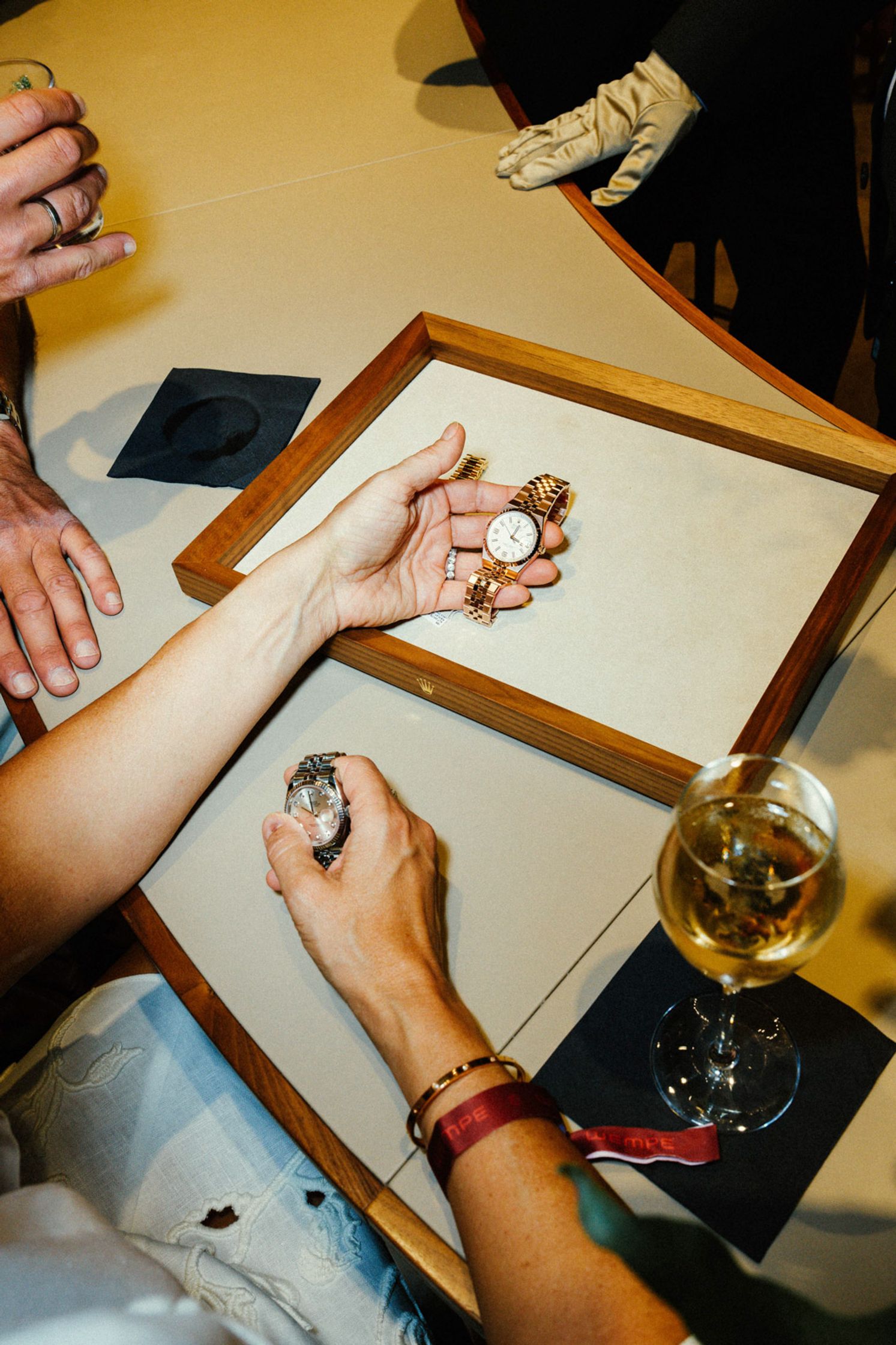 Hände beim Betrachten von Rolex-Uhren auf einem Präsentationstablett, ein Weinglas daneben, entspannter Luxus-Event in der Rolex Boutique Berlin