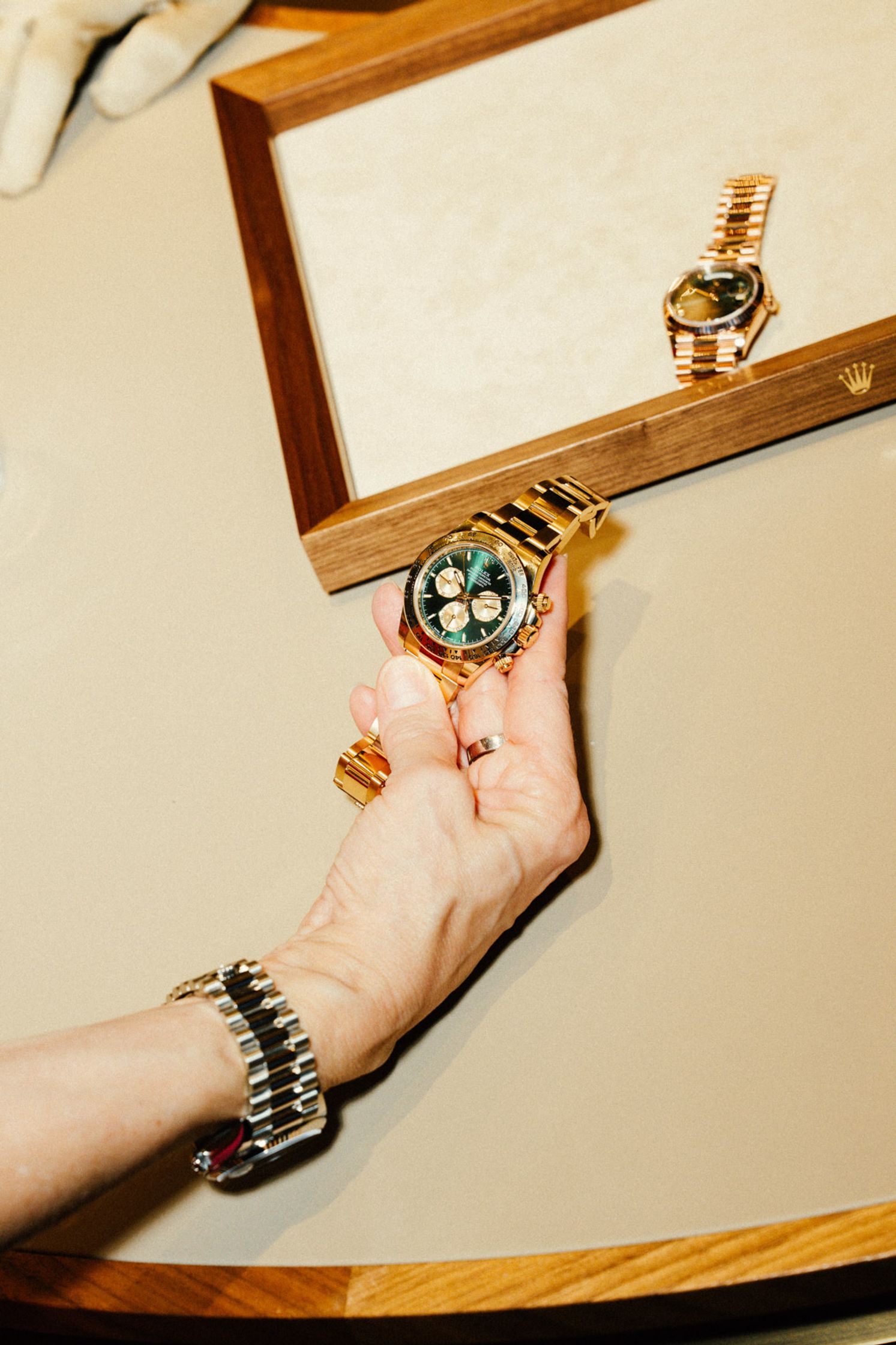 Hand mit Armband hält eine goldene Rolex-Uhr über dem Präsentationstablett, weitere Uhr im Hintergrund sichtbar, elegante Detail-Aufnahme Rolex Boutique Berlin