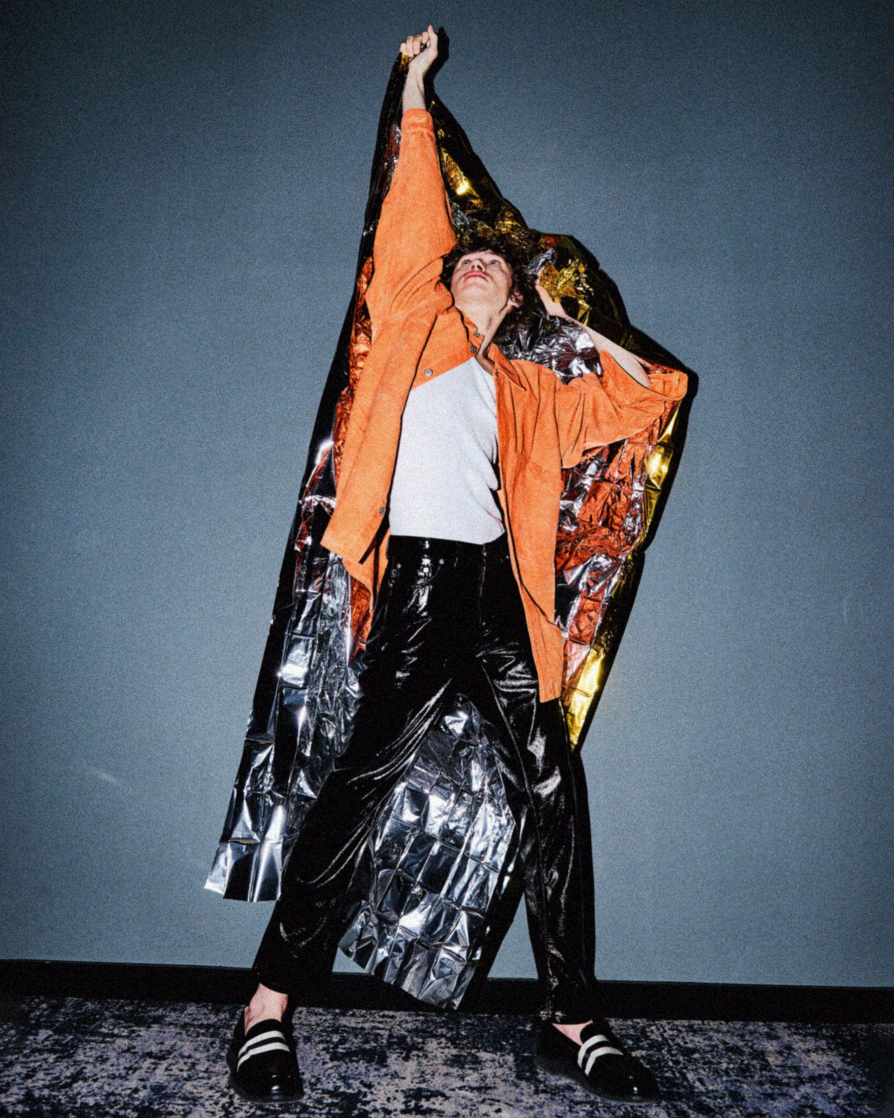 a woman in an orange jacket and black pants is posing for a photo
