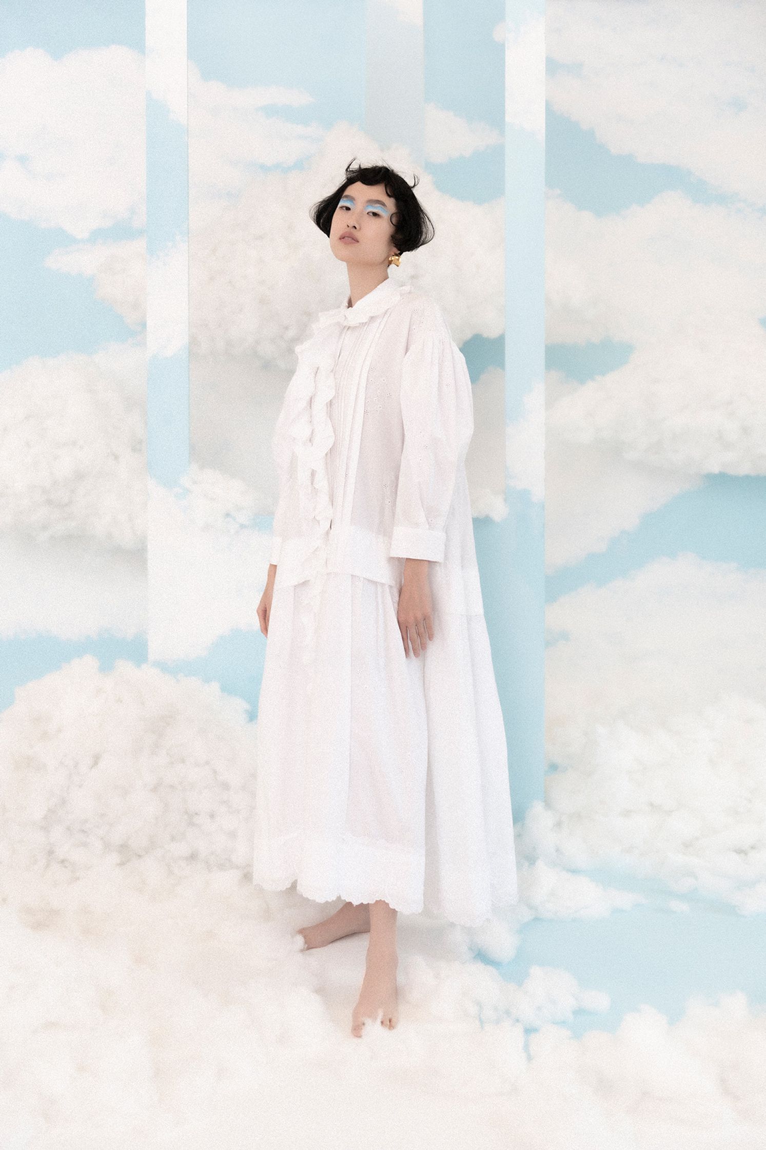 a woman in a white dress standing in front of clouds