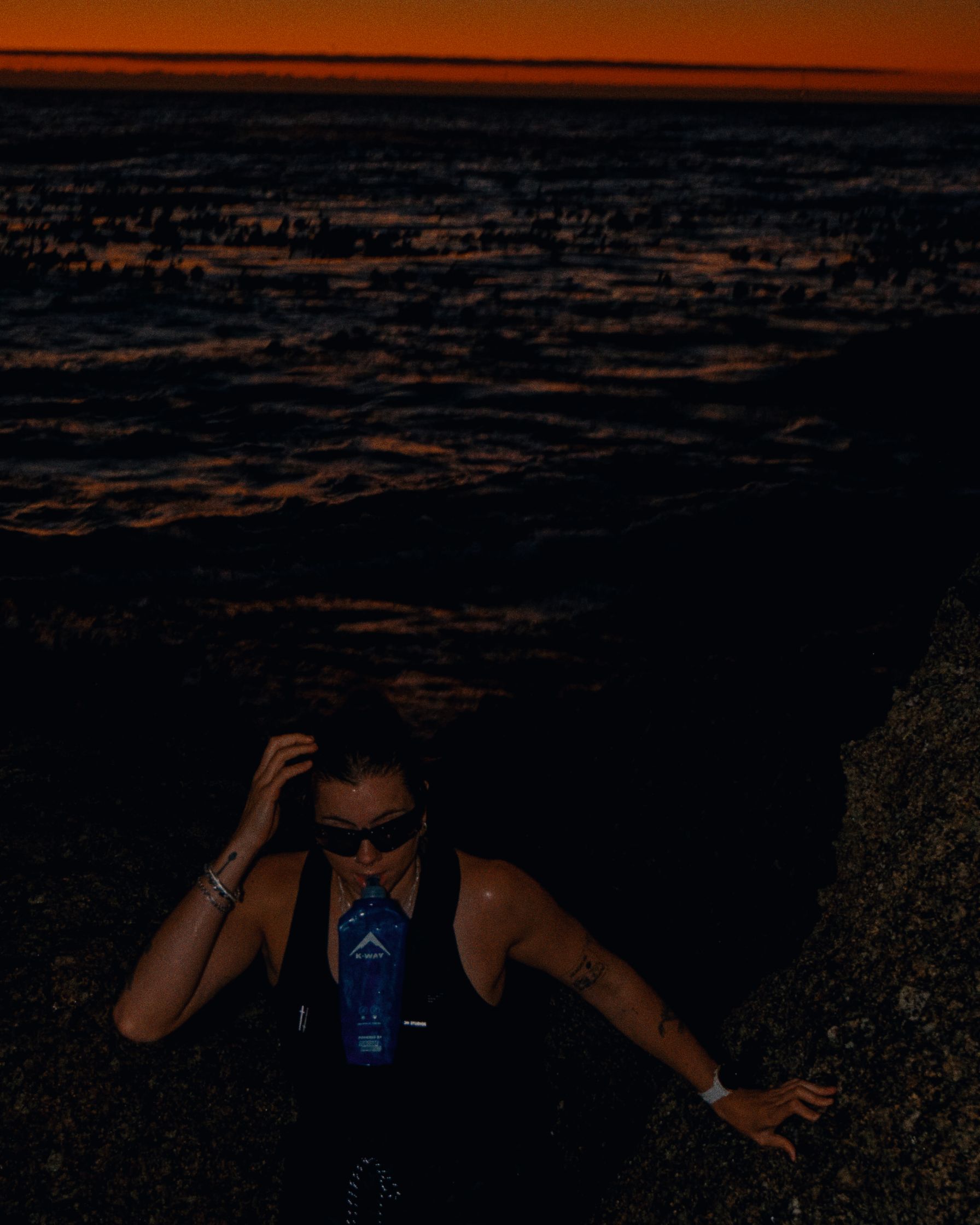 a woman is standing on a rock at sunset