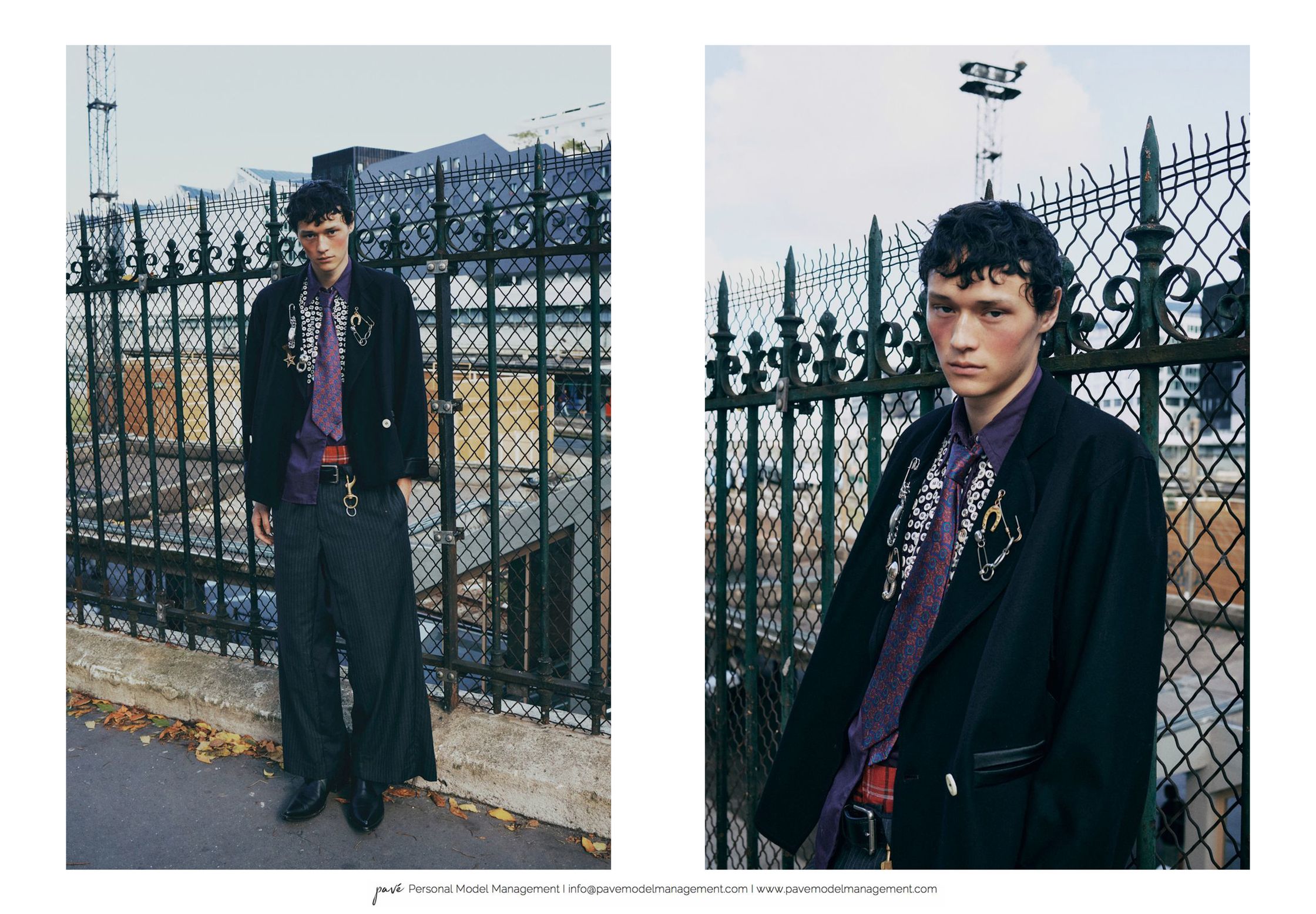 A model with short curly hair poses in two shots wearing a black jacket and striped pants in front of a metal fence.