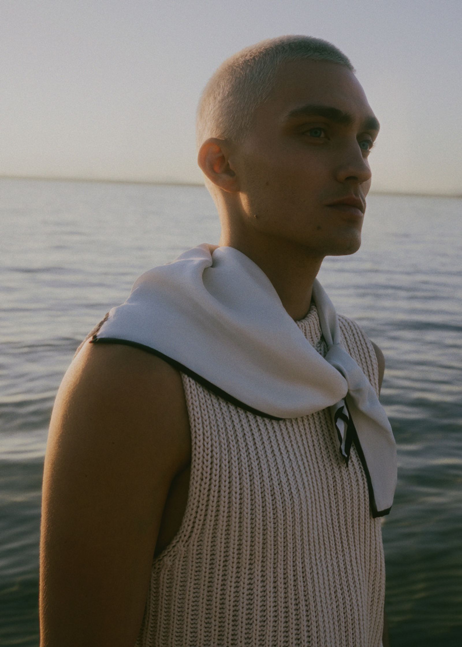 a man with a shaved head standing by the water