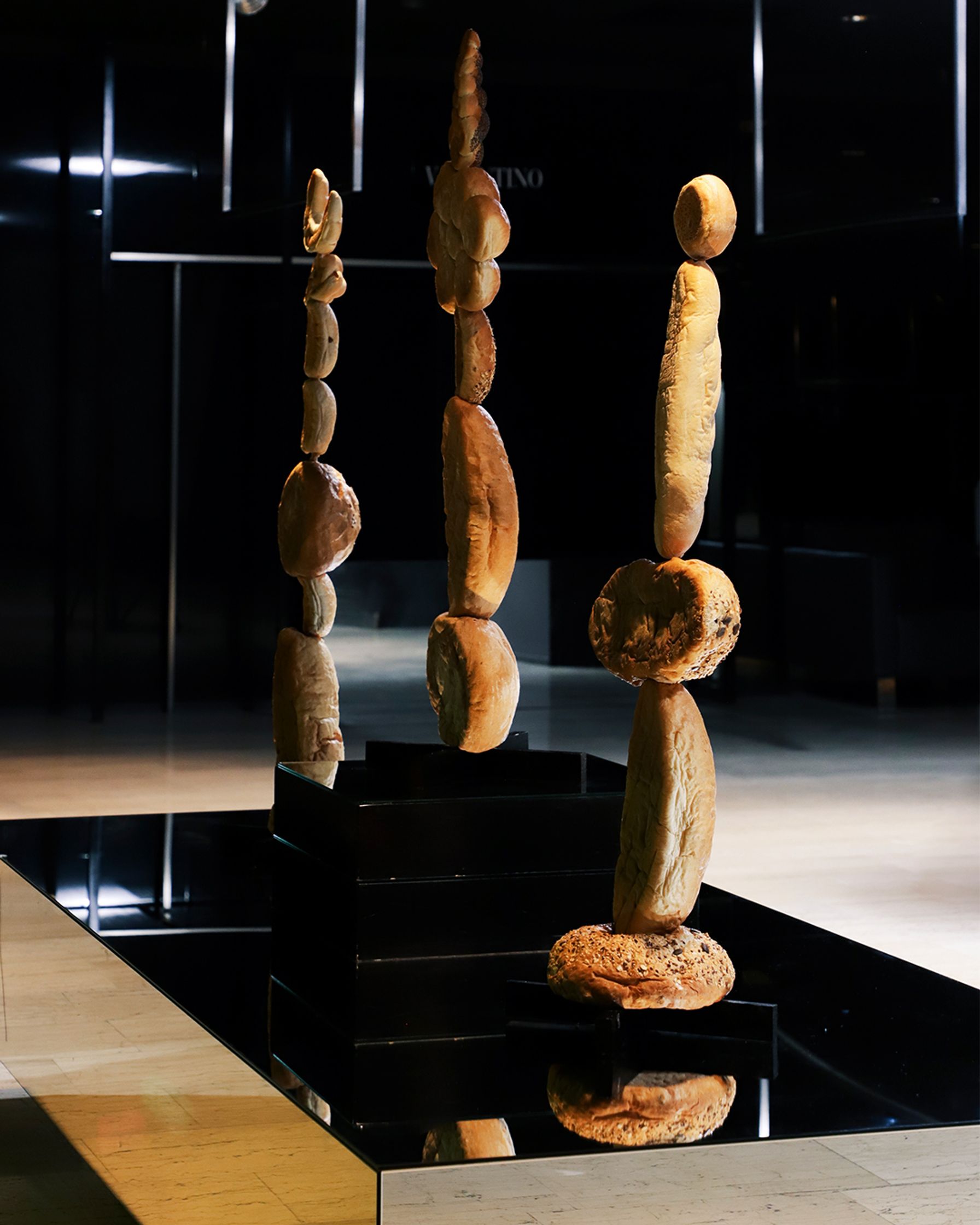Sculptures of bread loaves stacked in columns and displayed on a black reflective surface.