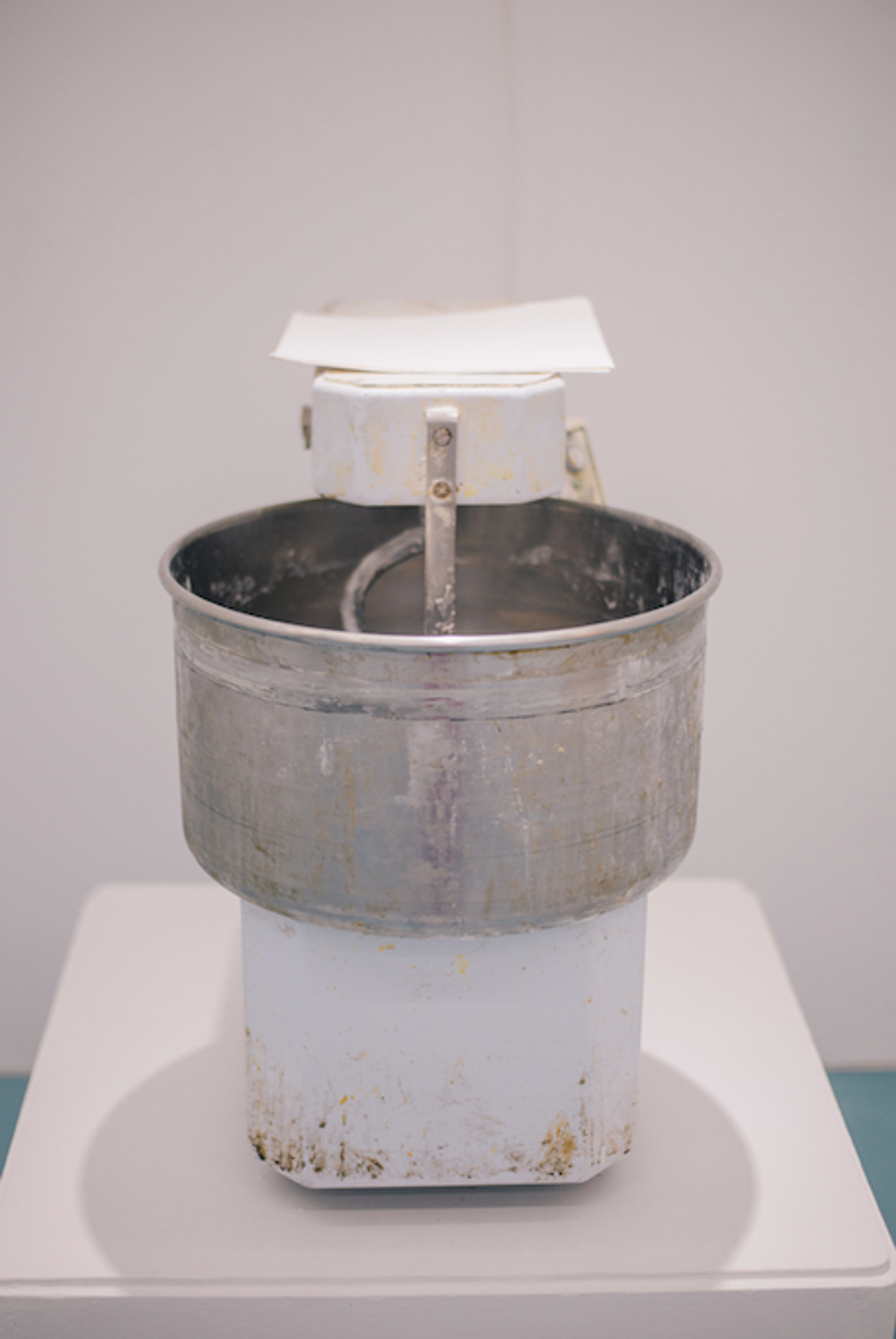 A used kitchen mixer with a large silver bowl and white base on a white counter.