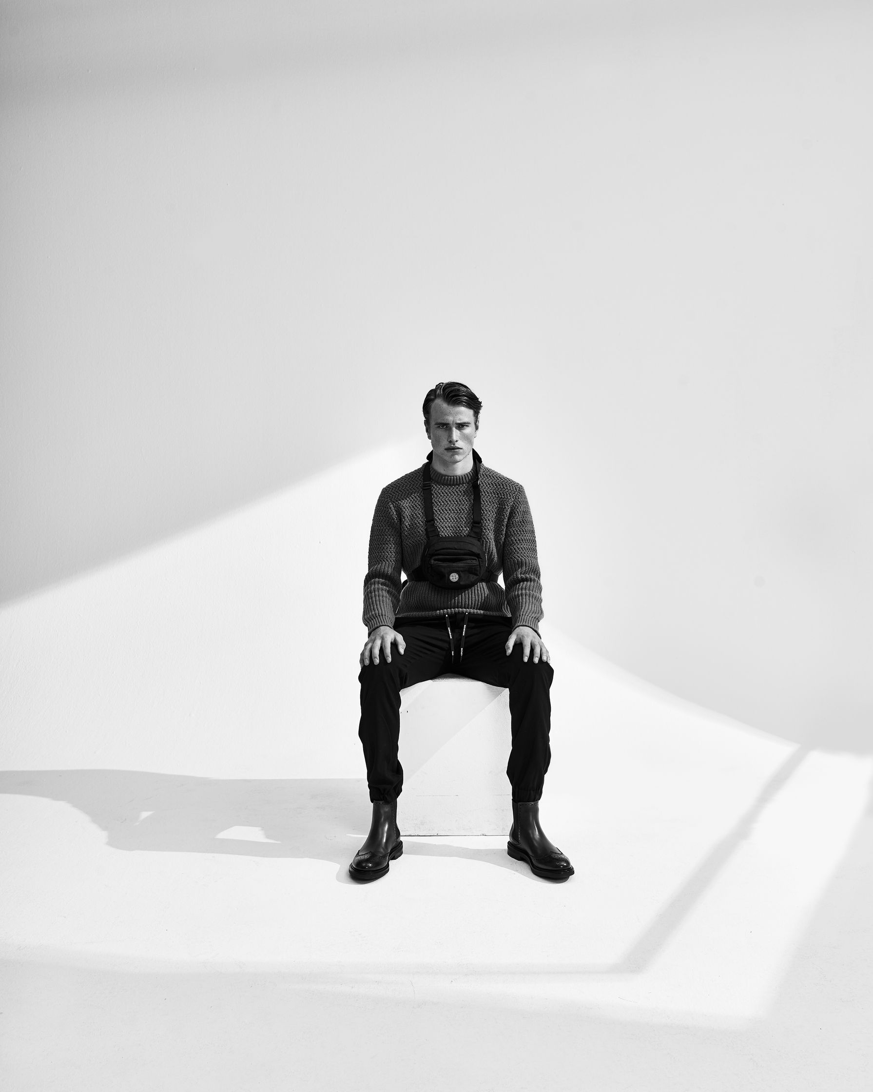 a black and white photo of a man sitting on a white box