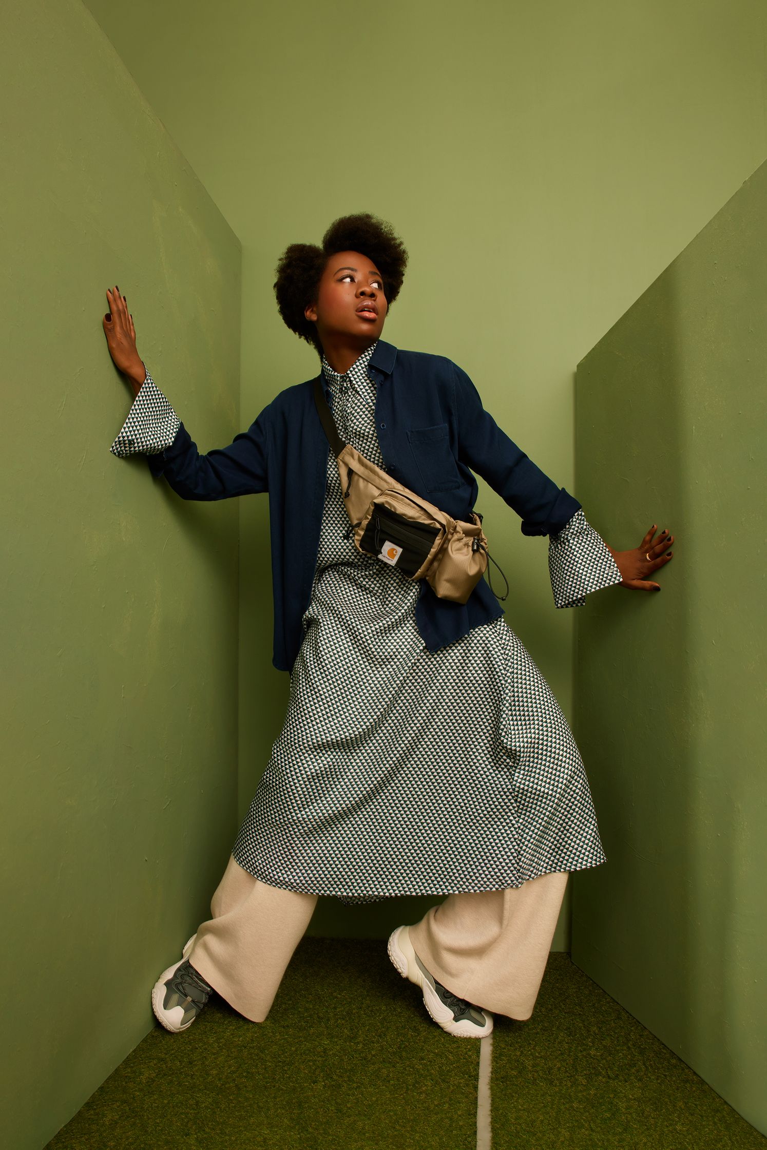 a black woman in a skirt and blazer posing in front of a green wall