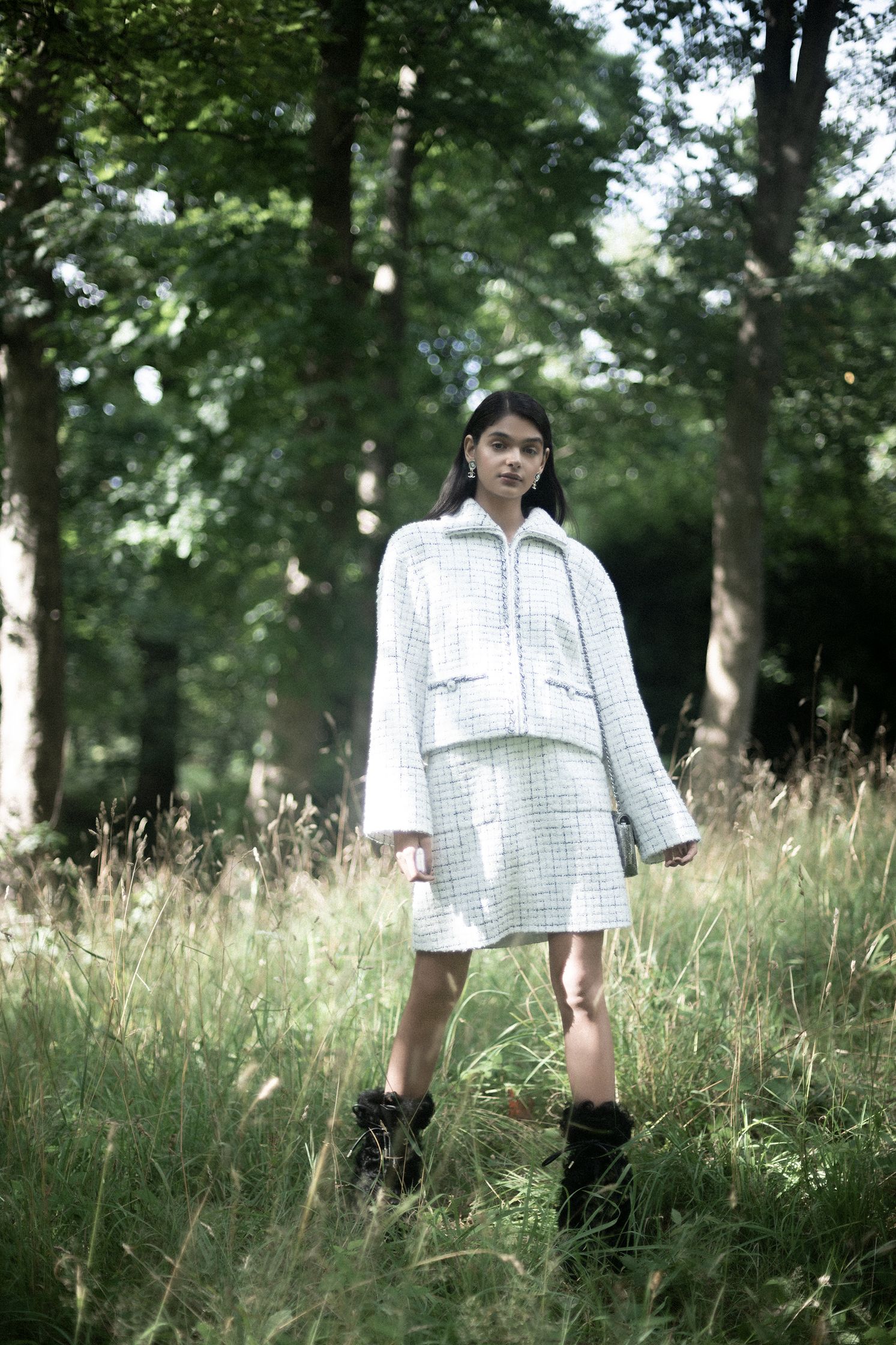 a woman in a white tweed jacket standing in the woods