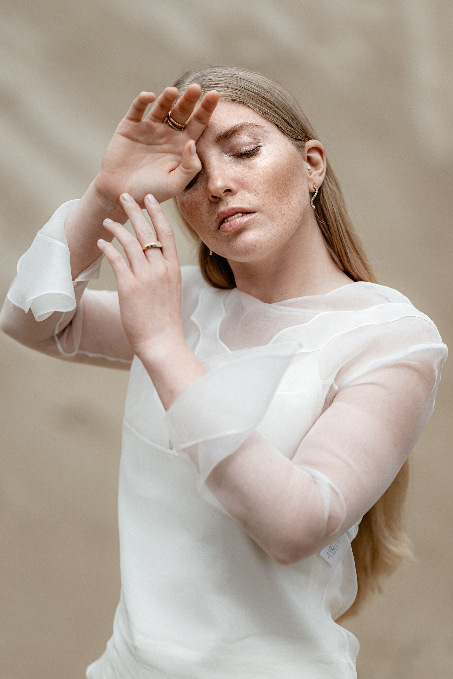 a woman in a white dress posing with her hands on her face with maren jewellery, earings, rings