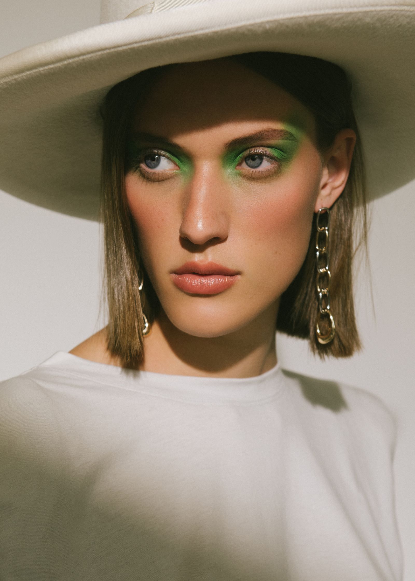 a model wearing a white hat and green eye makeup