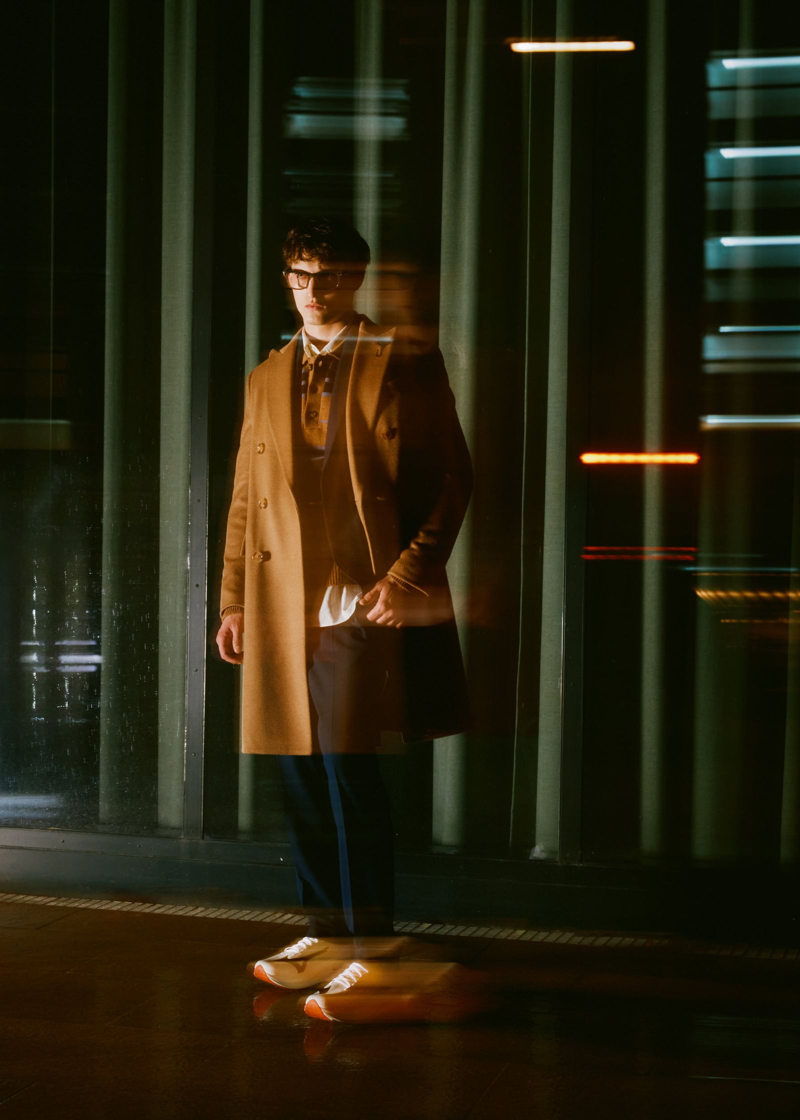 a man in a coat standing on a skateboard at night