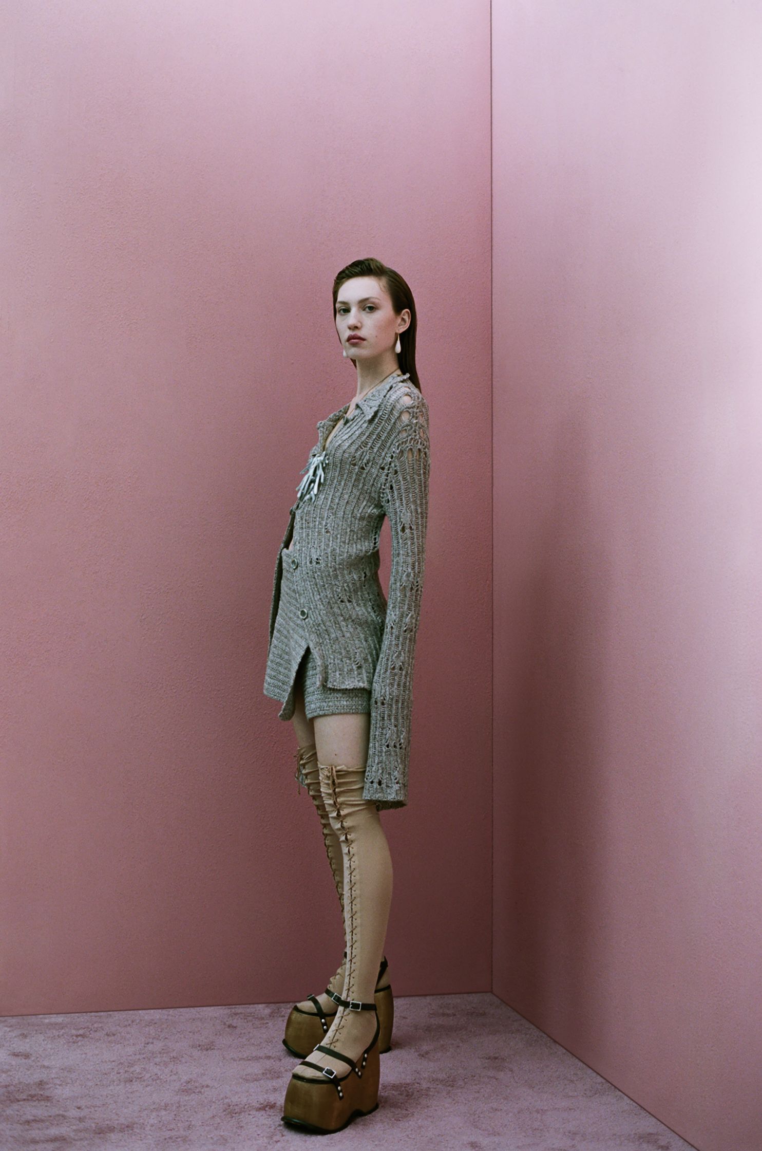 a woman in a sweater and stockings posing in a pink room