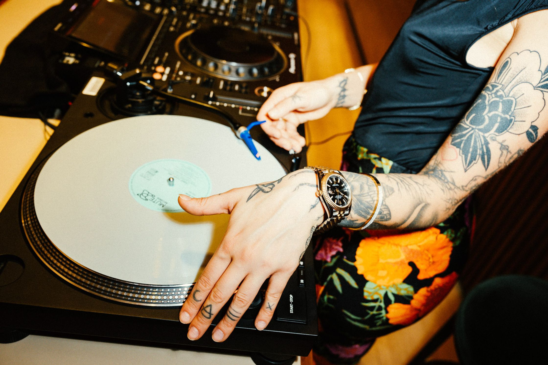 DJ mit tätowierten Armen und Rolex-Uhr am Handgelenk signiert eine Schallplatte auf einem Plattenspieler, Lifestyle-Event Rolex Boutique Berlin