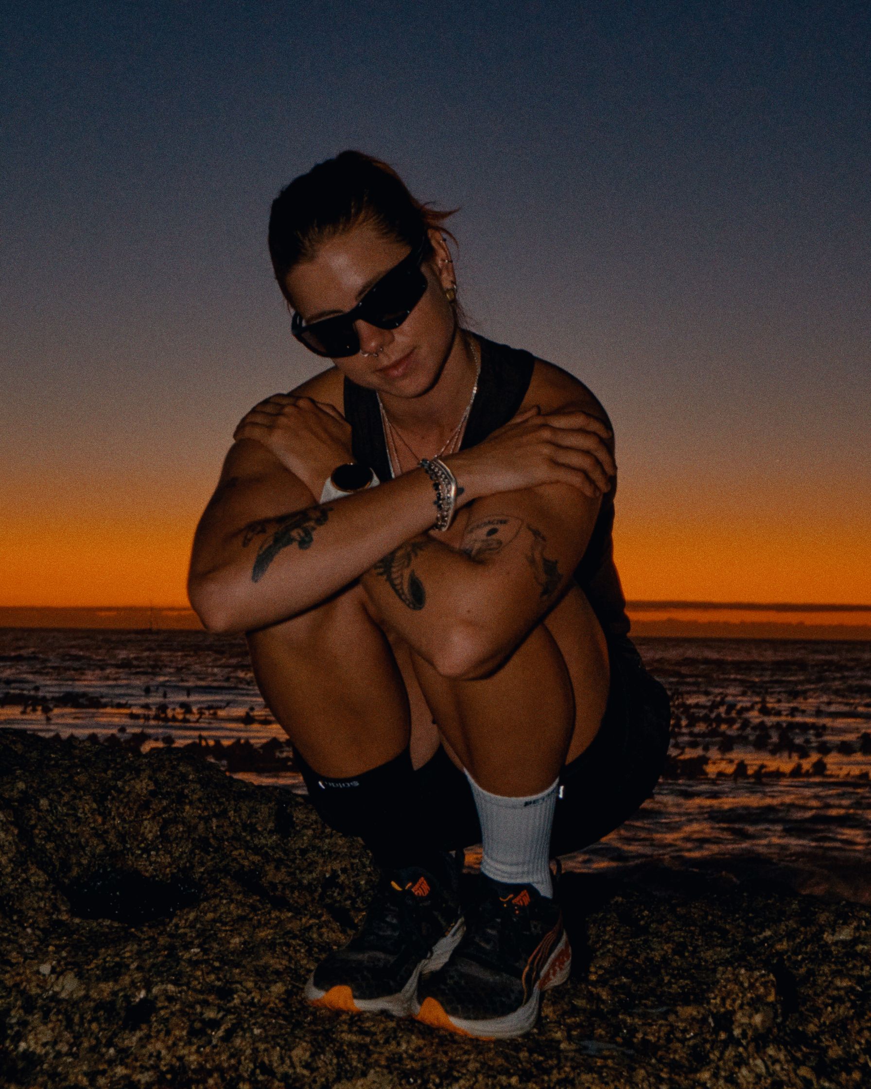 a woman crouching on rocks at sunset