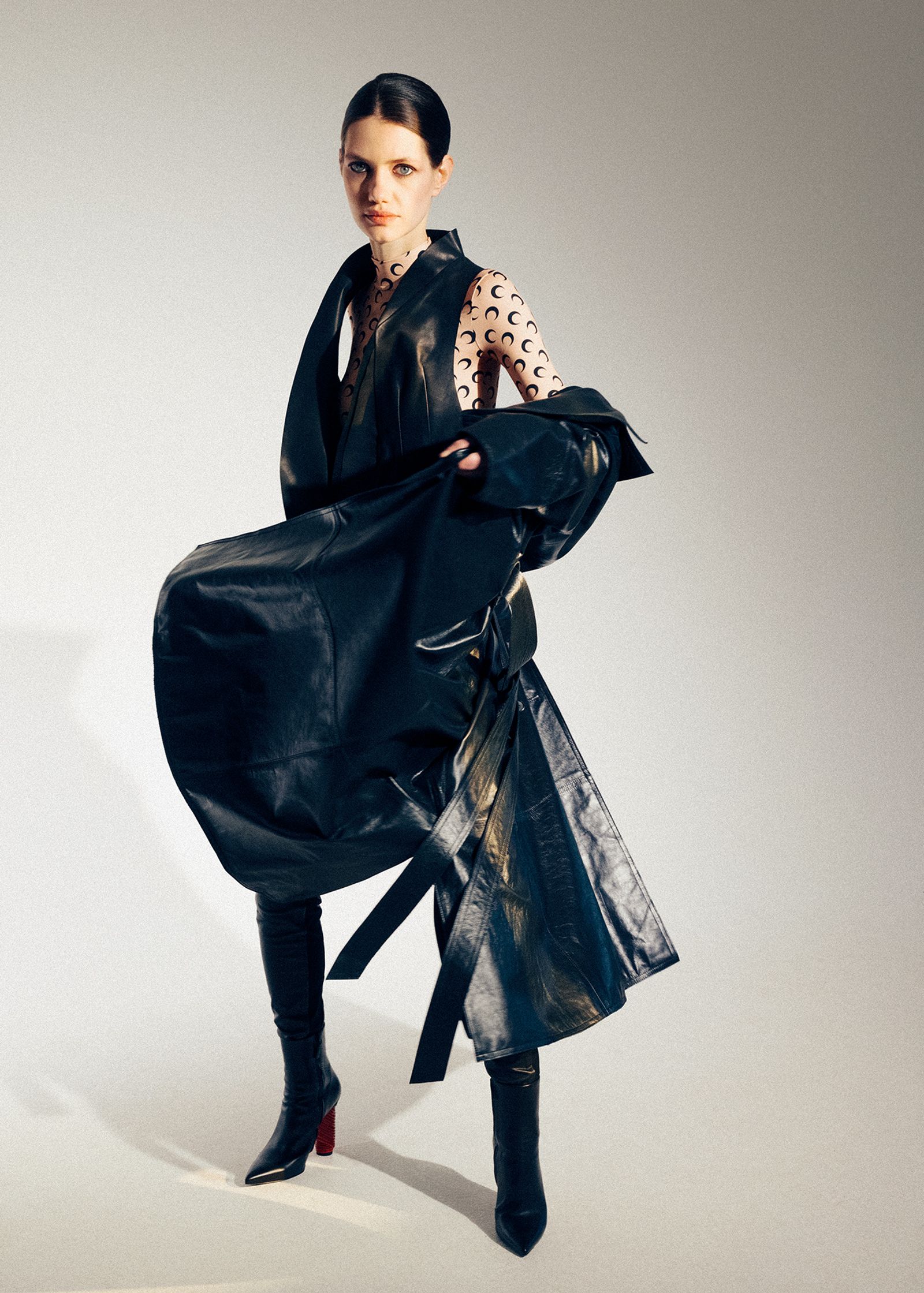 a woman in a black trench coat is posing in front of a white background