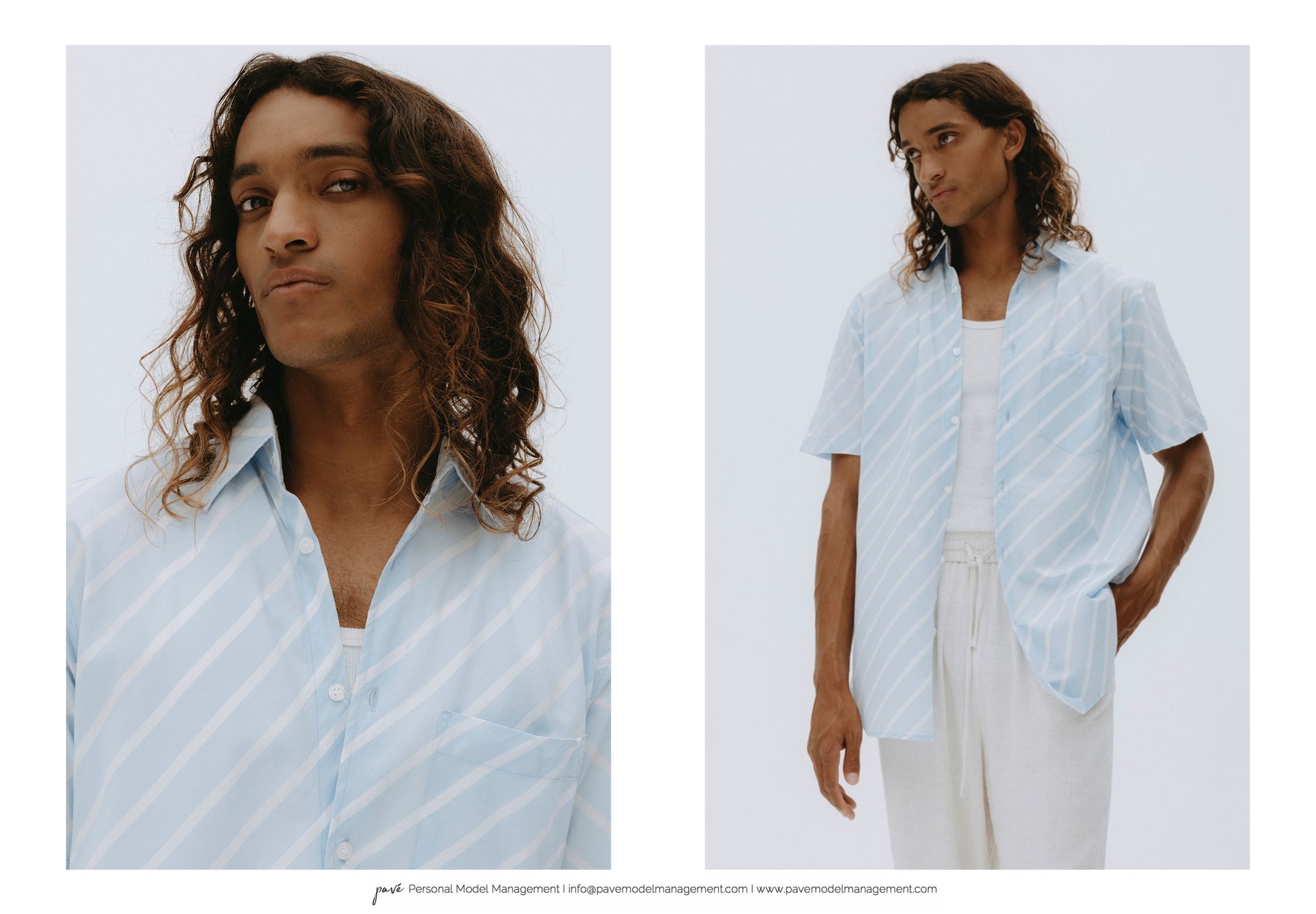 A man with long curly hair wears a light blue striped short-sleeved button-down shirt over a white tank top, paired with light-colored drawstring pants.