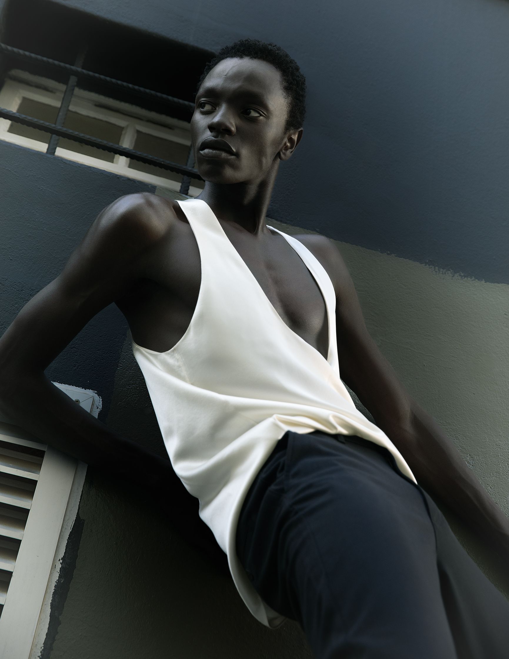 a man in a white tank top leaning against a wall