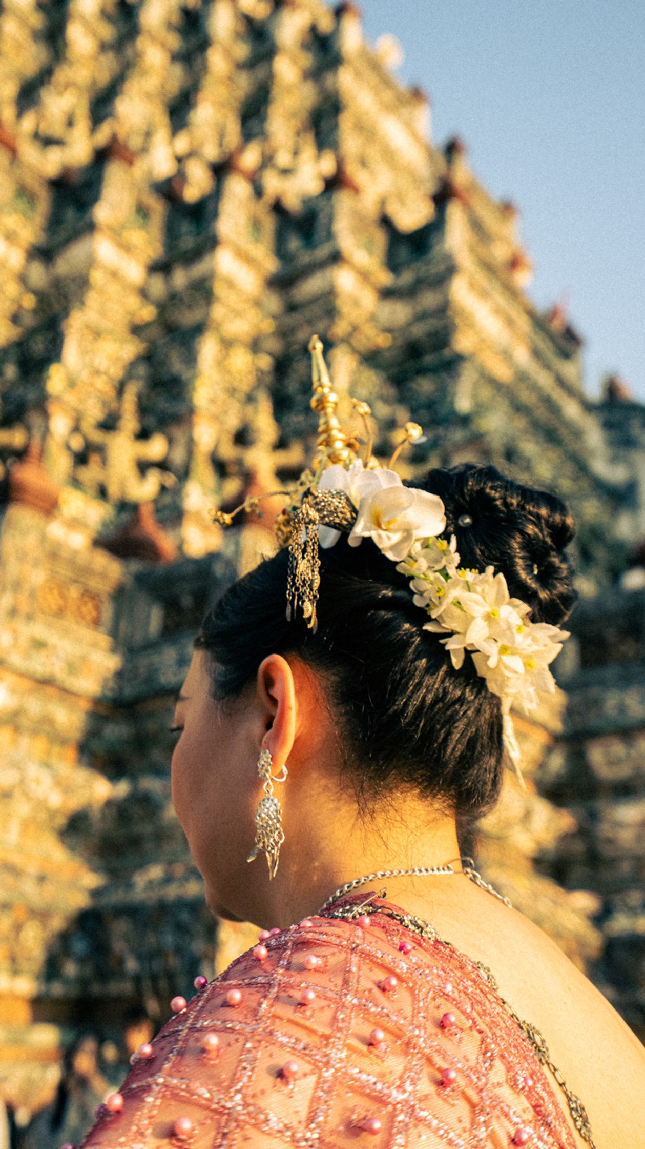 A woman in intricate traditional dress standing in front of a temple during the golden hour. Warm light enhancing the architectural details and the cultural heritage moment.