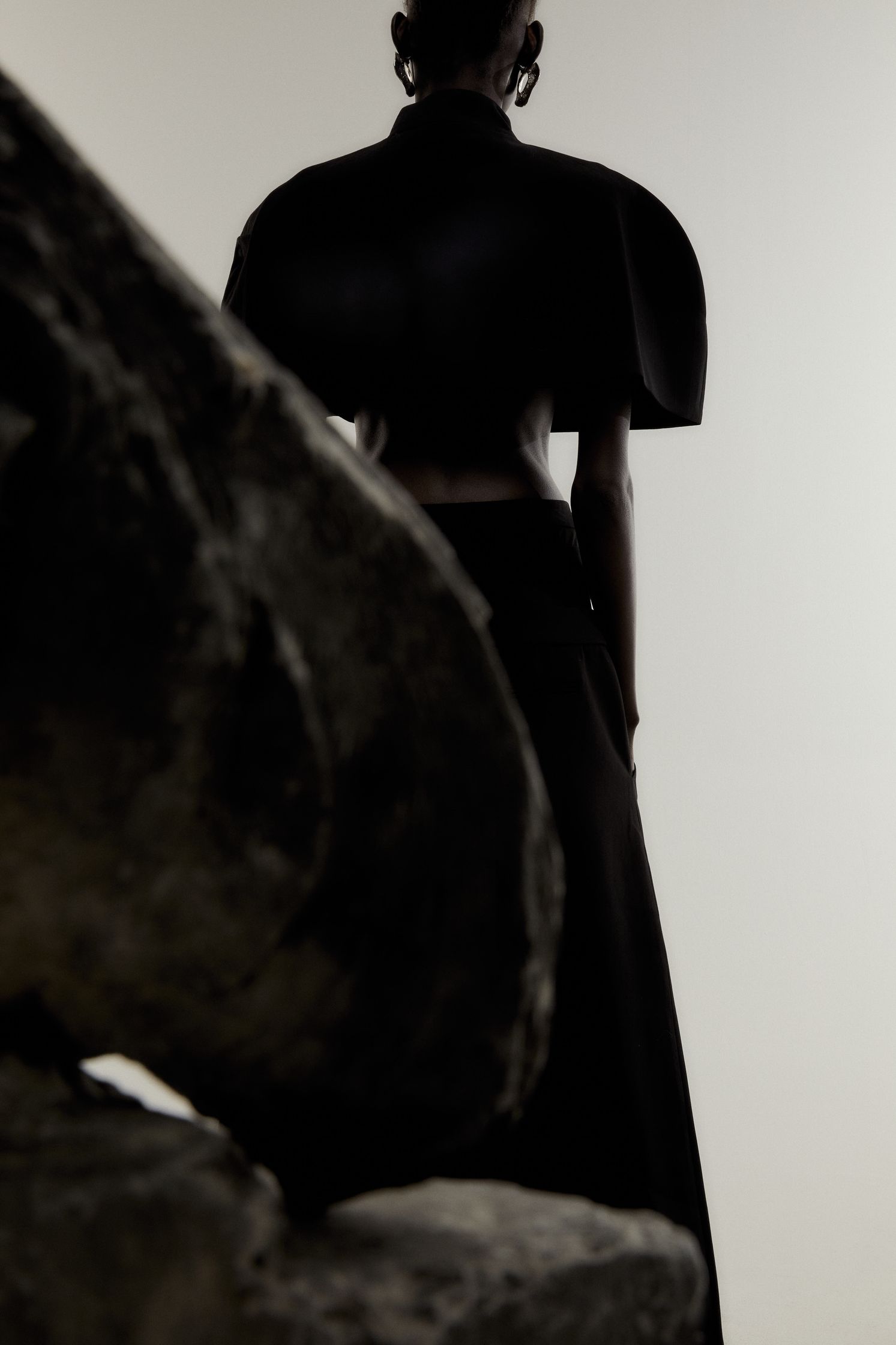 a woman in a black dress standing next to a rock