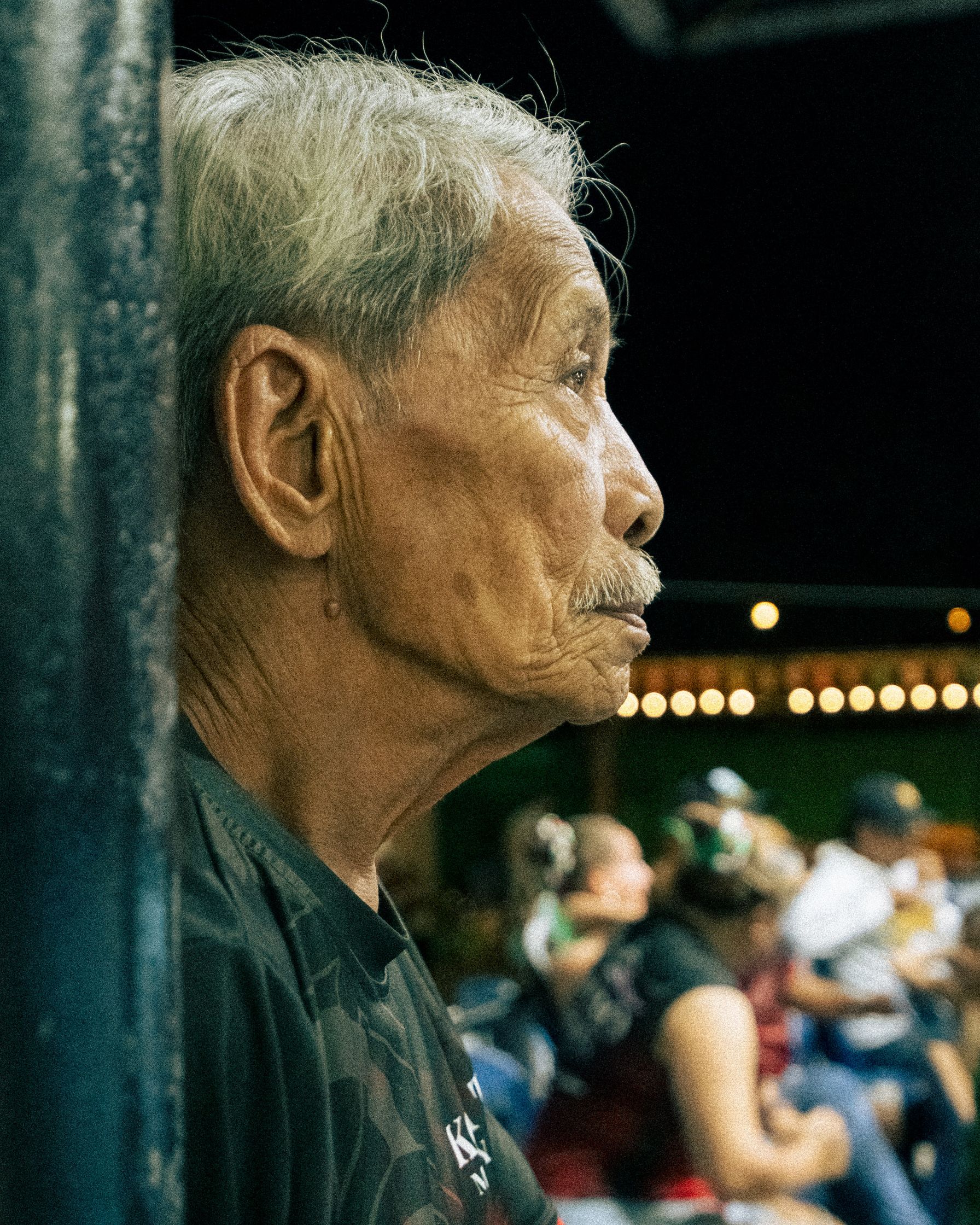 A poignant documentary shot of a Muay Thai Kru (master) watching his student perform the ceremonial dance with pride and focus. Capturing the spirit of lineage and mentorship at Koh Tao.