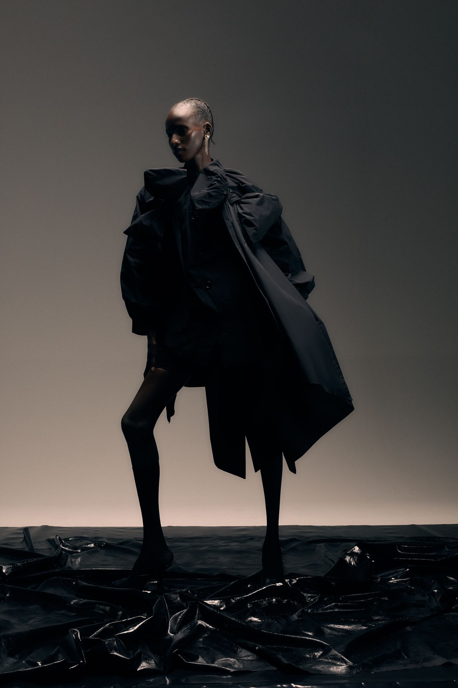 a woman in a black coat standing on a black background