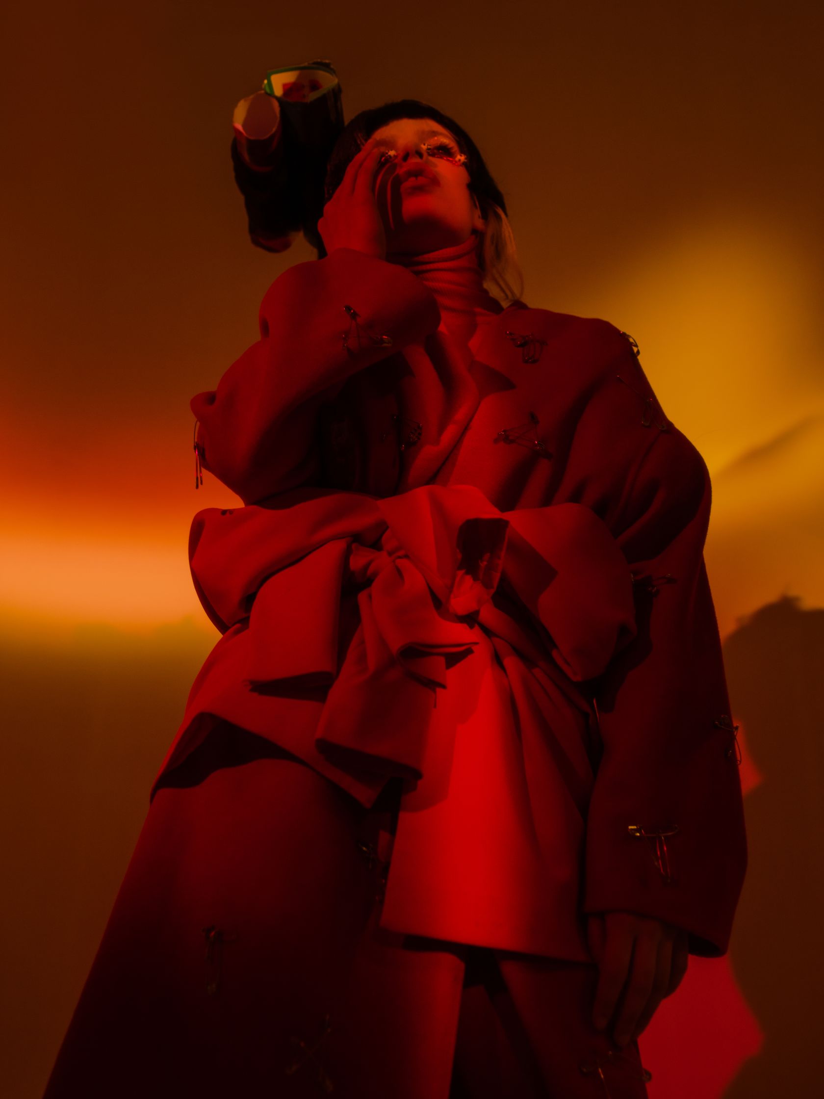 a woman in a red coat is posing in front of an orange light